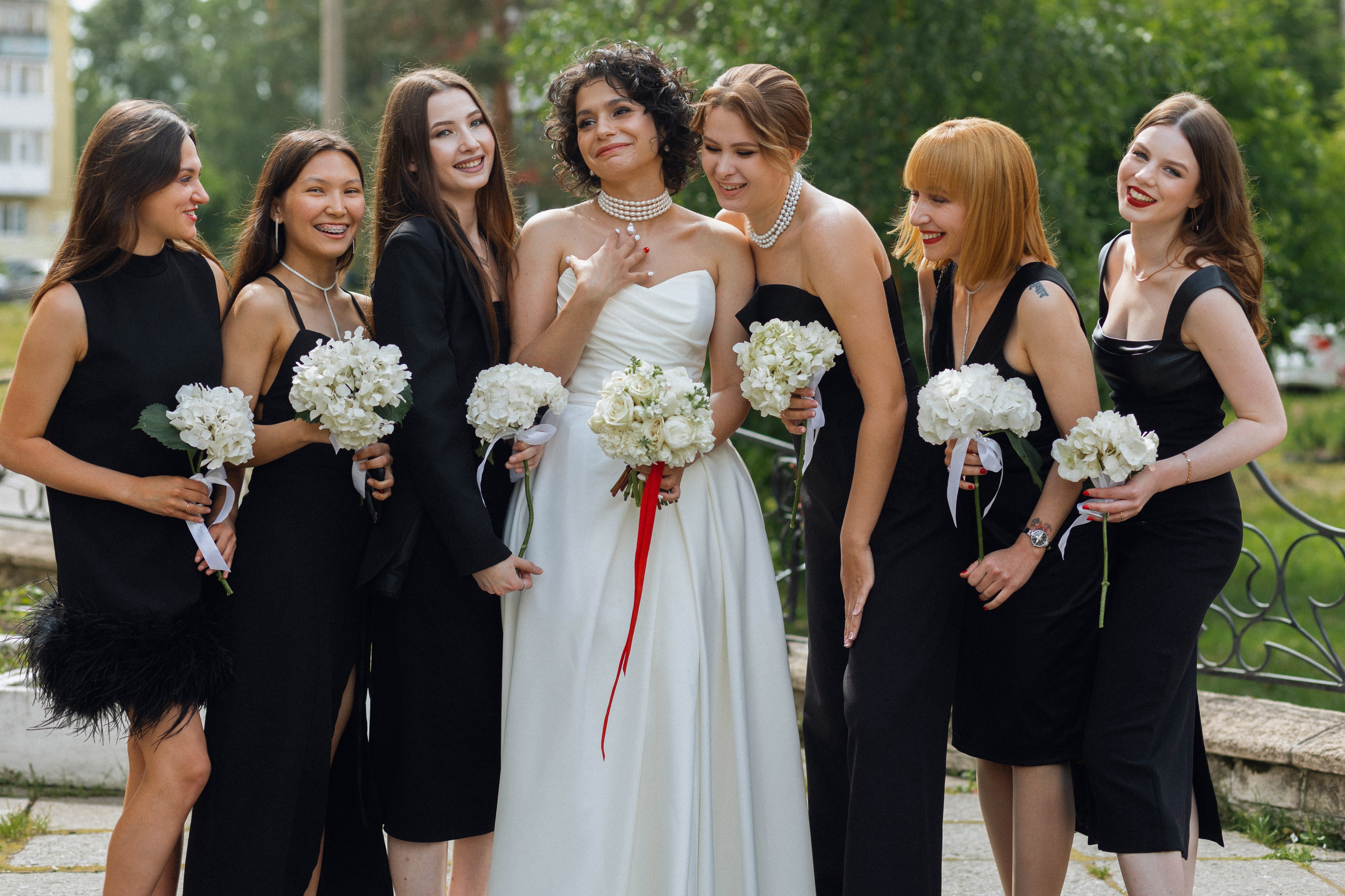 Контраст элегантности: подружки в черных шелковых платьях рассматривают белоснежное атласное платье невесты от салона NATALIE L