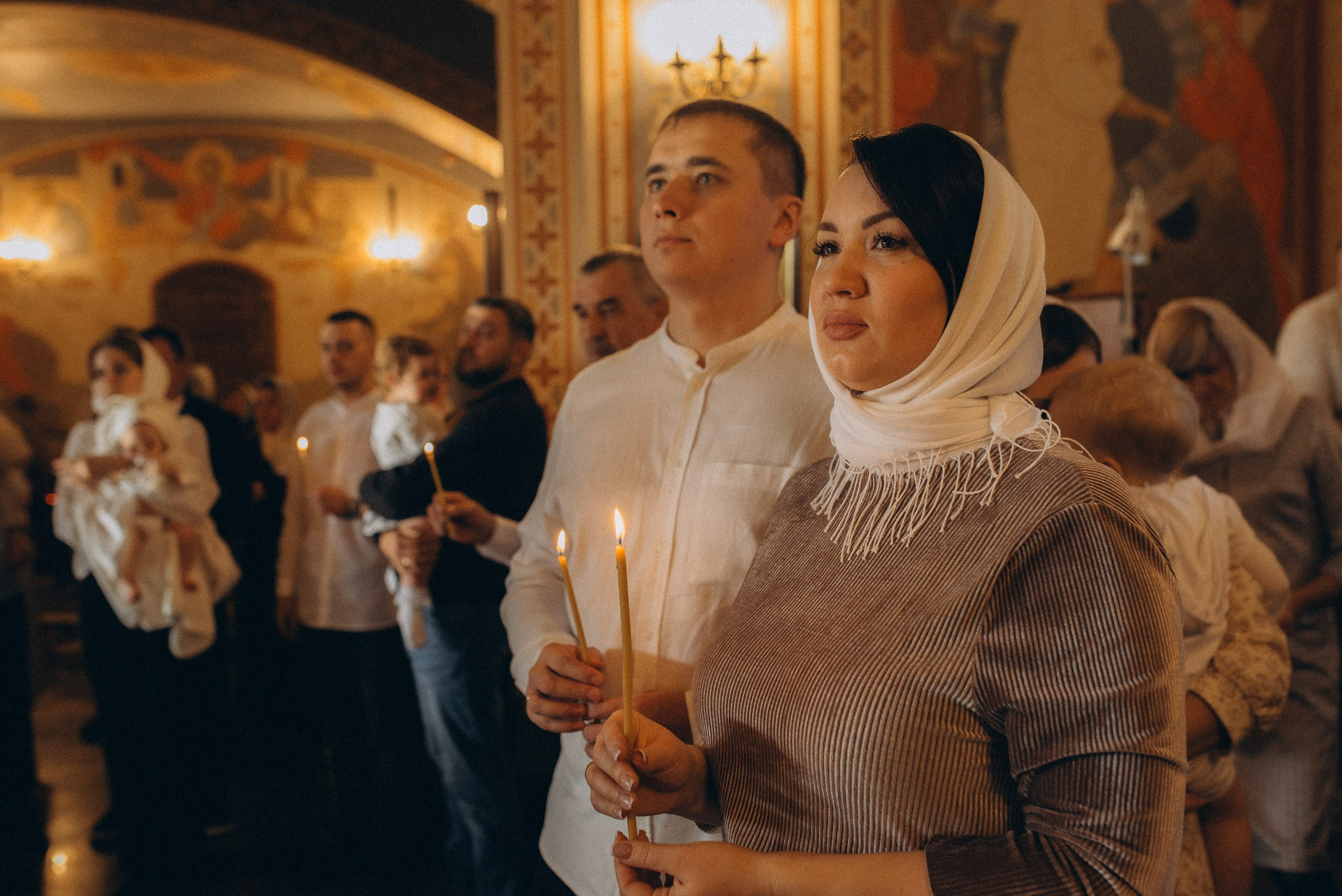 Профессиональная съемка в церкви — крестные родители со свечами внимательно слушают молитву священника