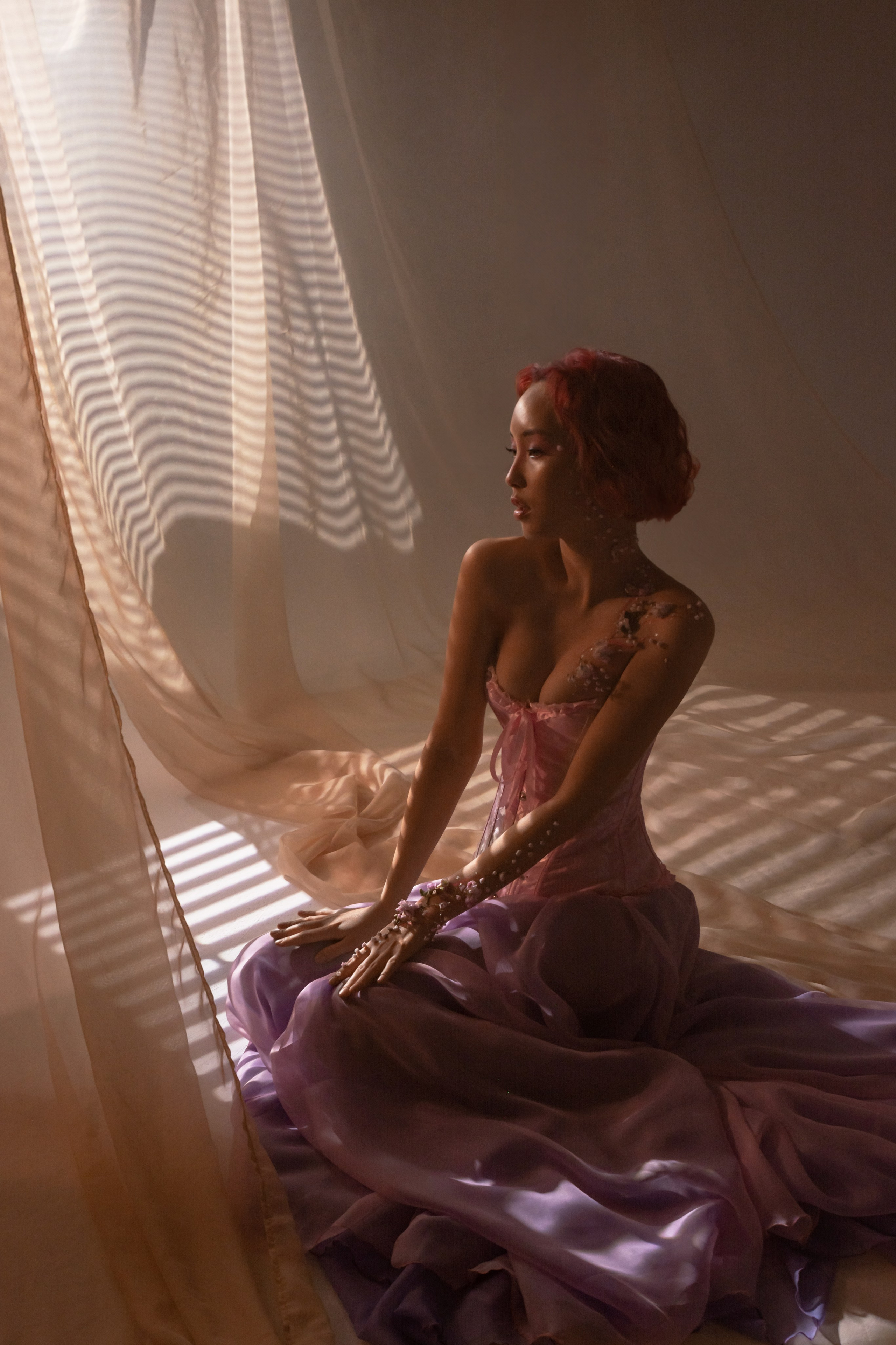 Окруженная потоками света из окна, стройная фигура в цветочном розовом наряде символизирует возрождение и обновление, знаменуя приход весны после зимней спячки.