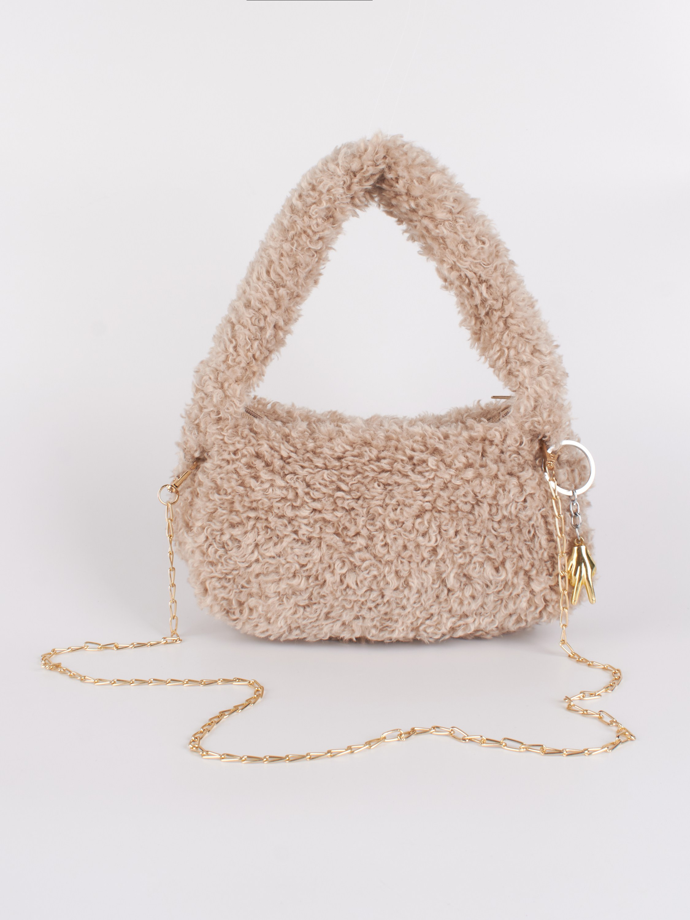 Пушистая сумка с брелоком в виде руки и золотой цепочкой на сером фоне
