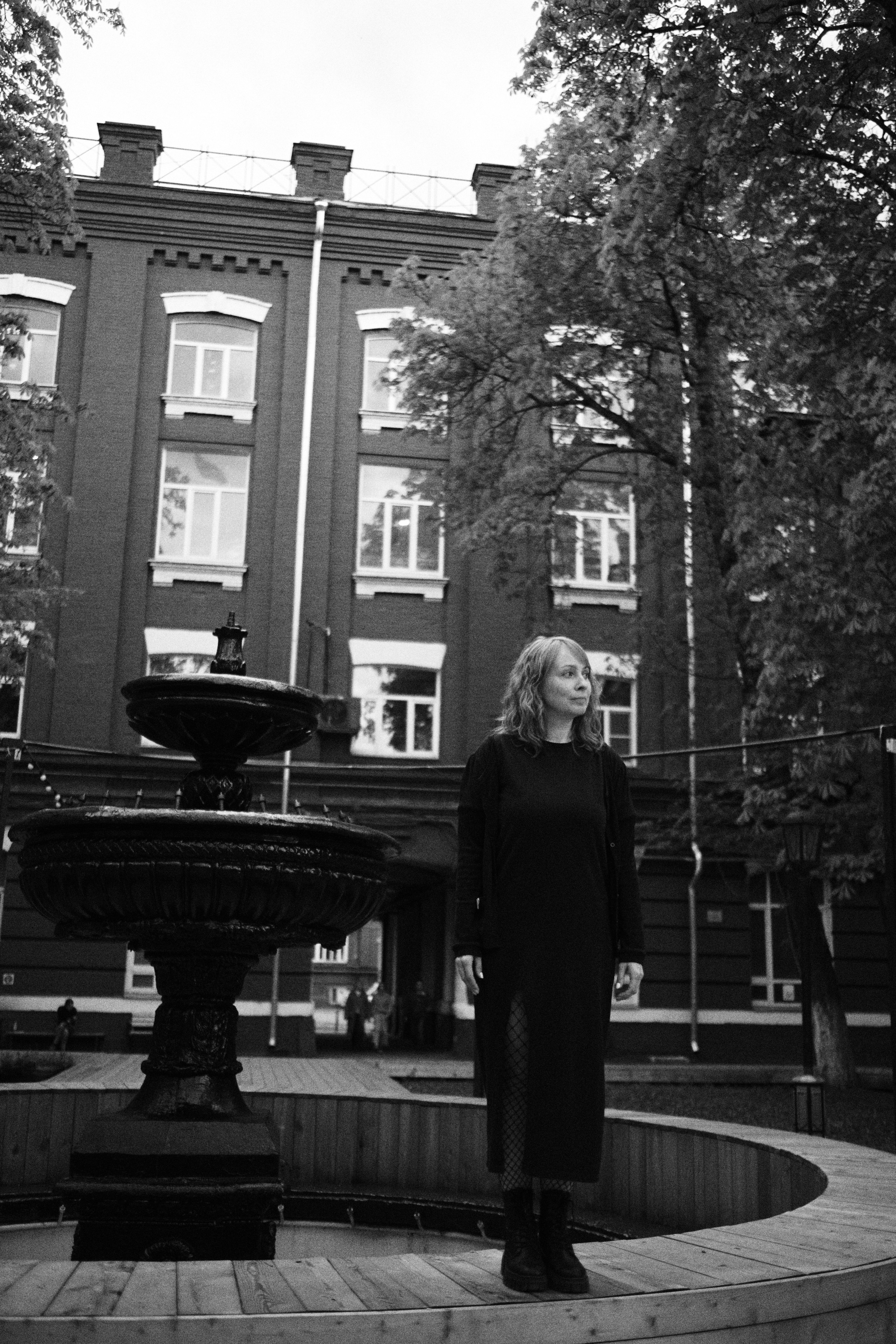 Женщина стоит во дворе здания у фонтана во весь рост