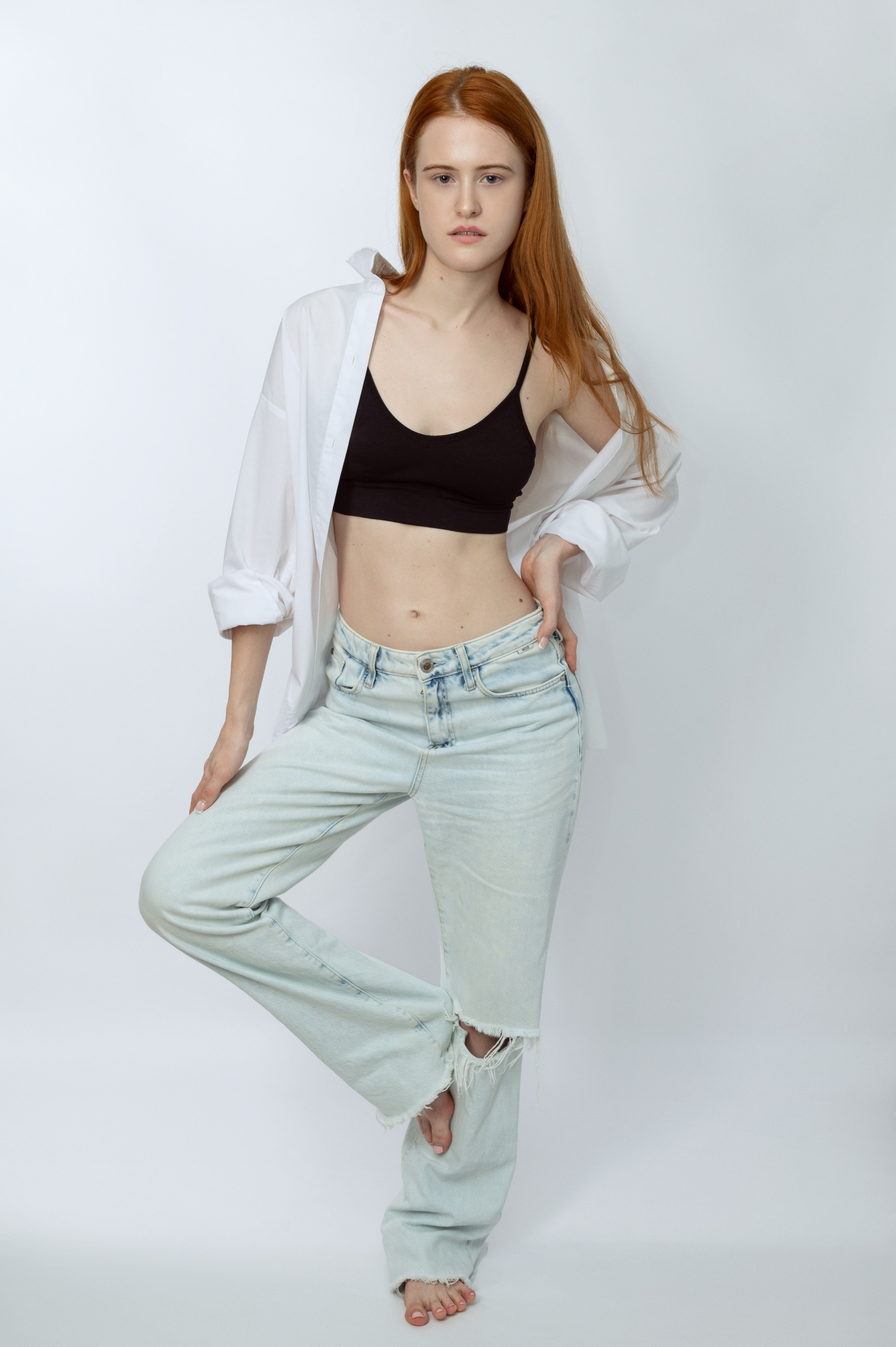 Рыжеволосая девушка-модель в белой рубашке и светлых джинсах на светлом фоне. Модельные тесты