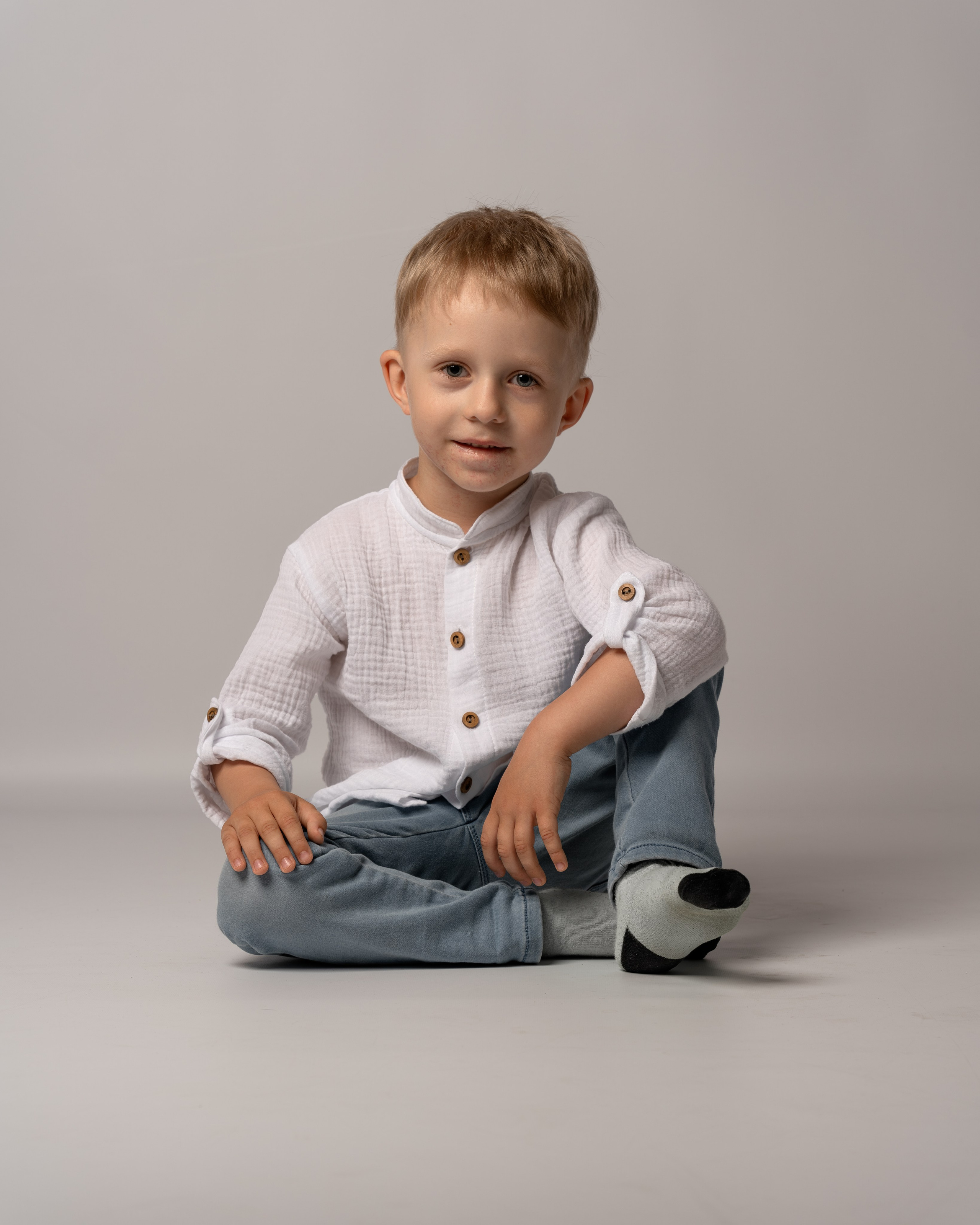 Студийная фотосессия. Детский портрет. Мальчик в рубашке и джинсах сидит на полу