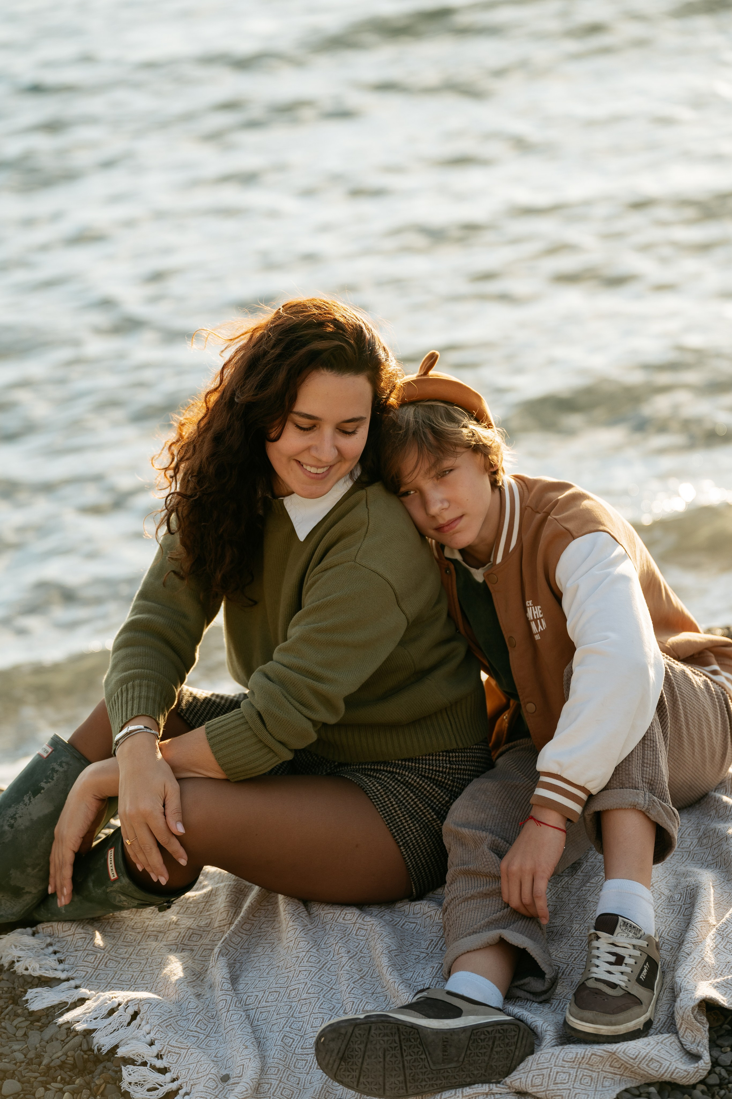 Портрет счастливой семьи на фотосессии в Новороссийске. Все вместе на большом валуне, на заднем плане — волны Черного моря.