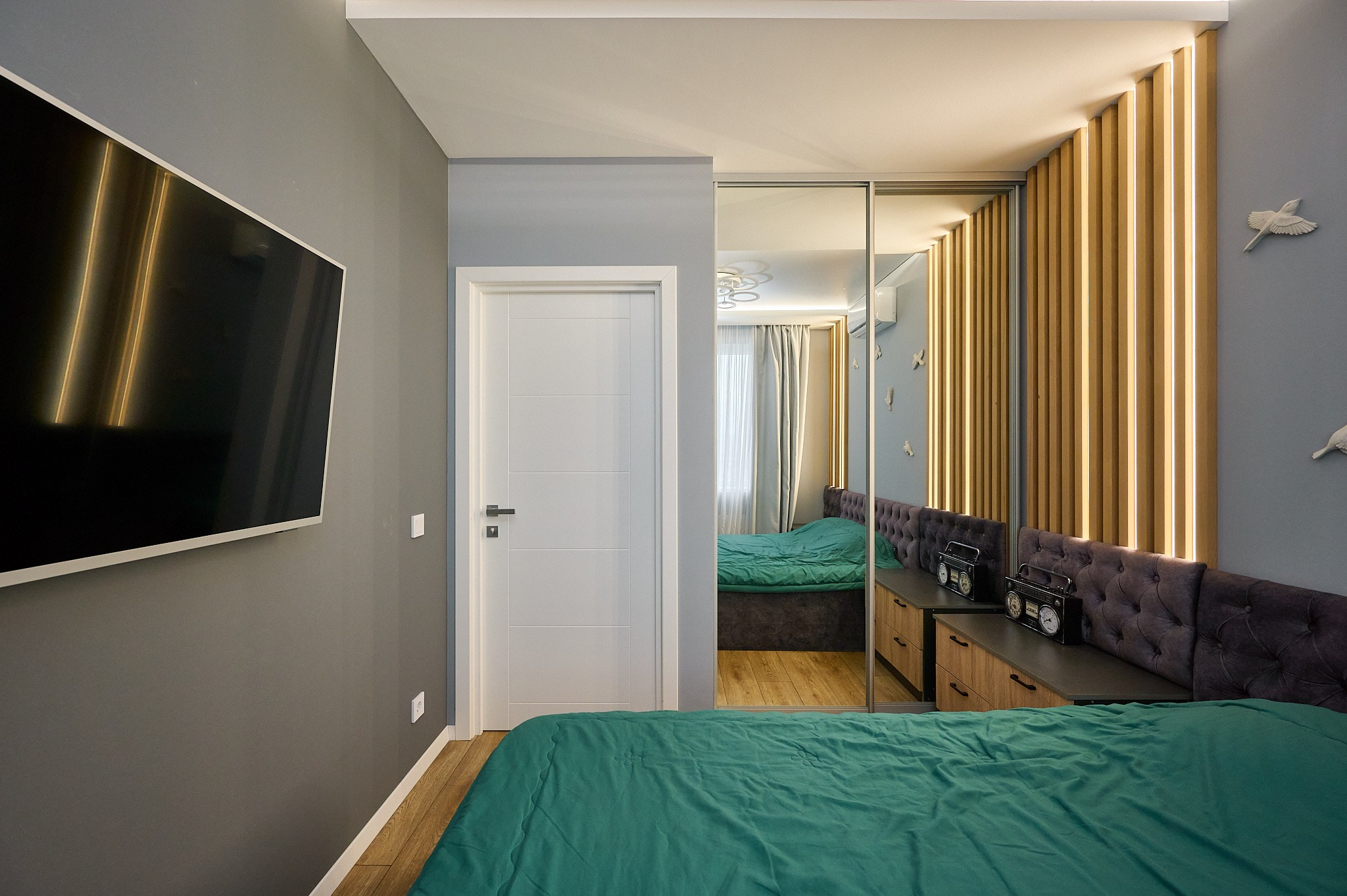 комната кровать тумбы у кровати шкаф с зеркалами телевизор серые шторы