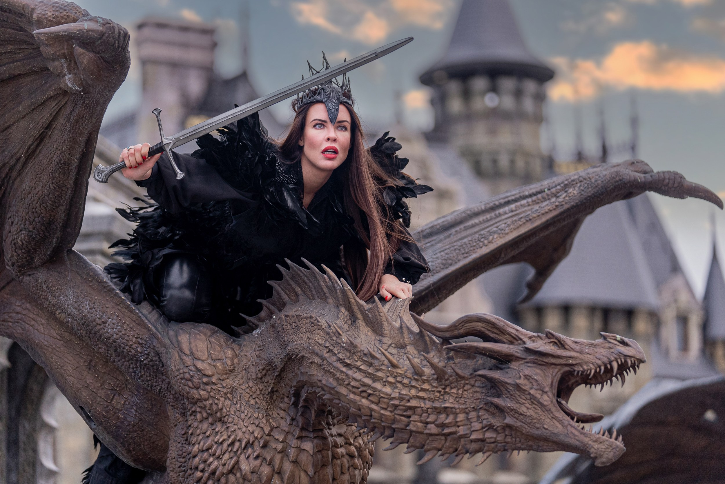 Модель в тёмном костюме верхом на скульптуре дракона в замке Гарибальди, придавая фотосессии эпичный и мистический колорит.