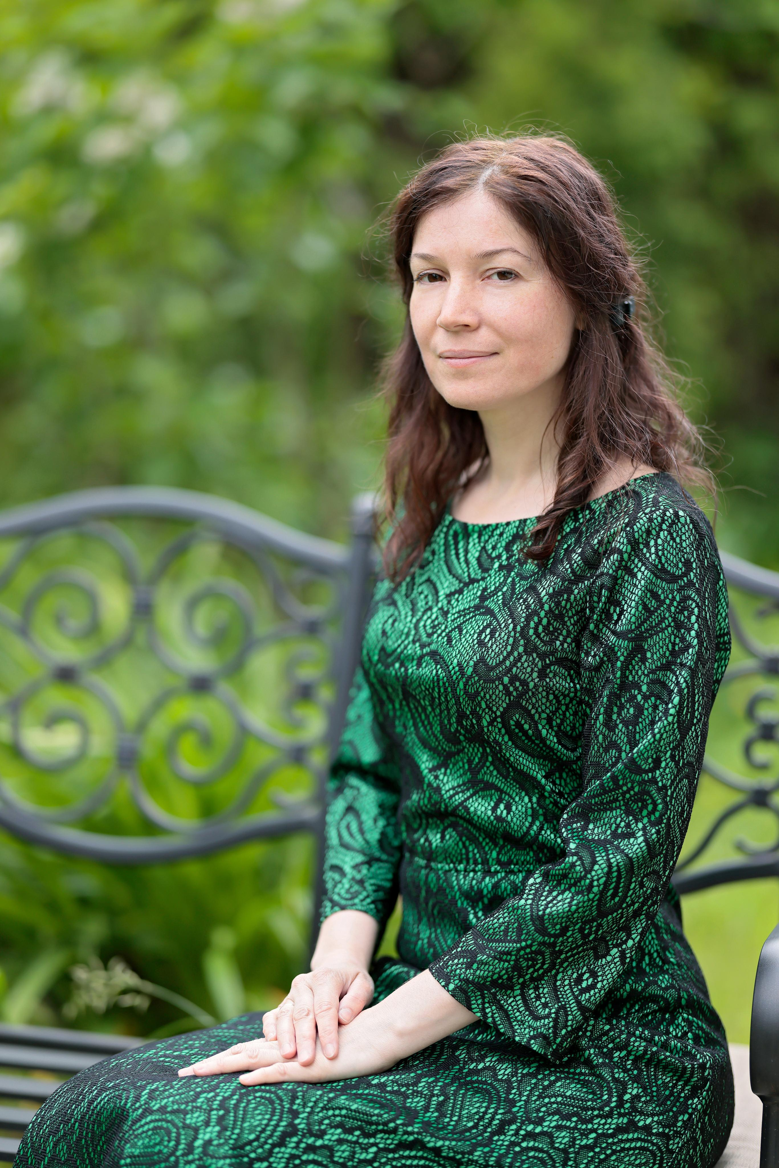 Портрет женщины в зелёном платье, сидящей на скамейке на фоне зелени.
