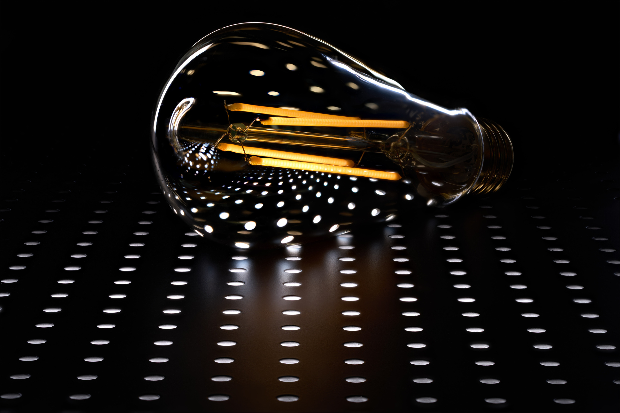 горящая  лампочка на фоне перфорированного отверстиями чёрного листа металла