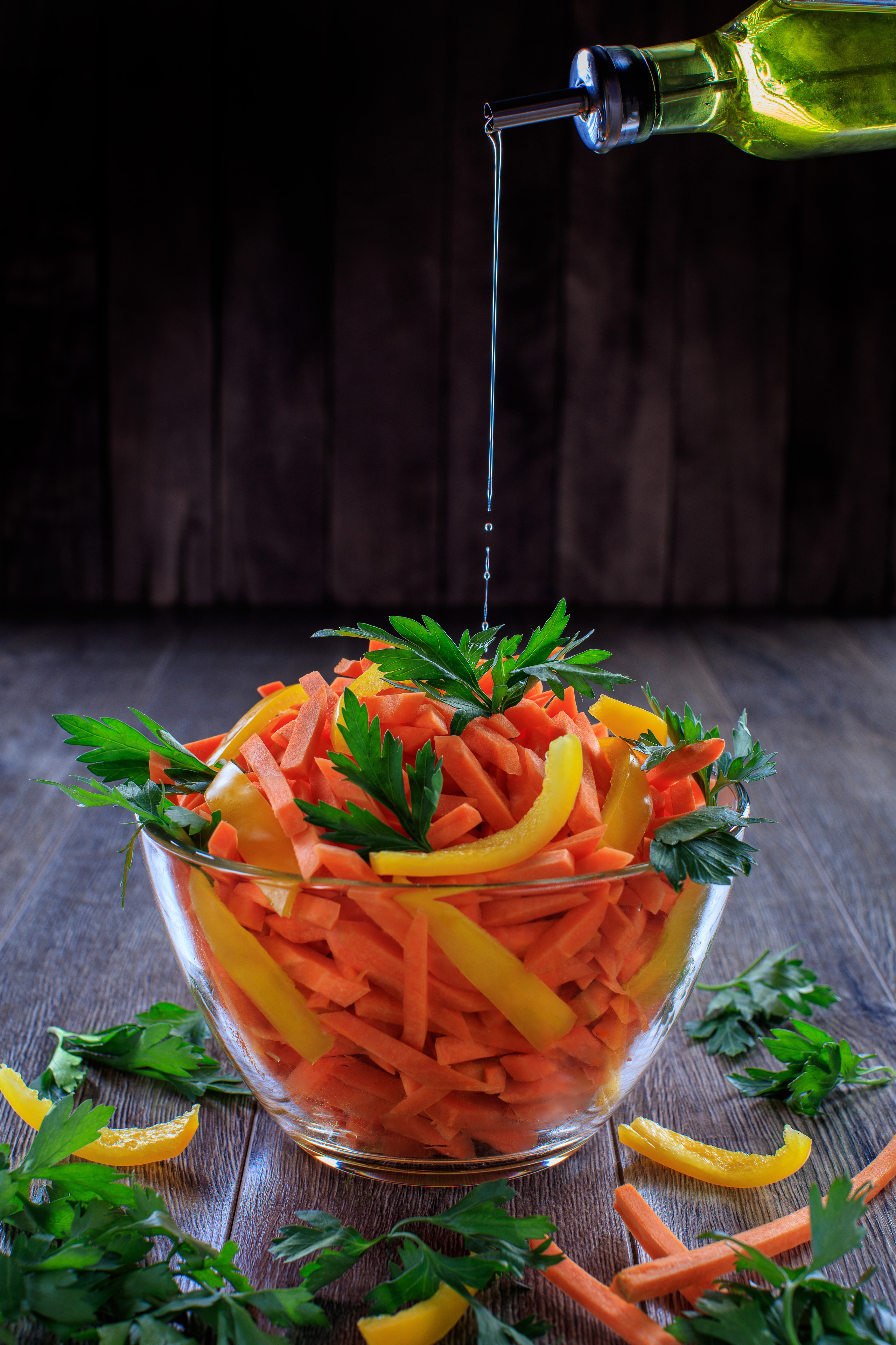 фото салата из моркови перца и зелени в стеклянной миске поливается из бутылки оливковым маслом