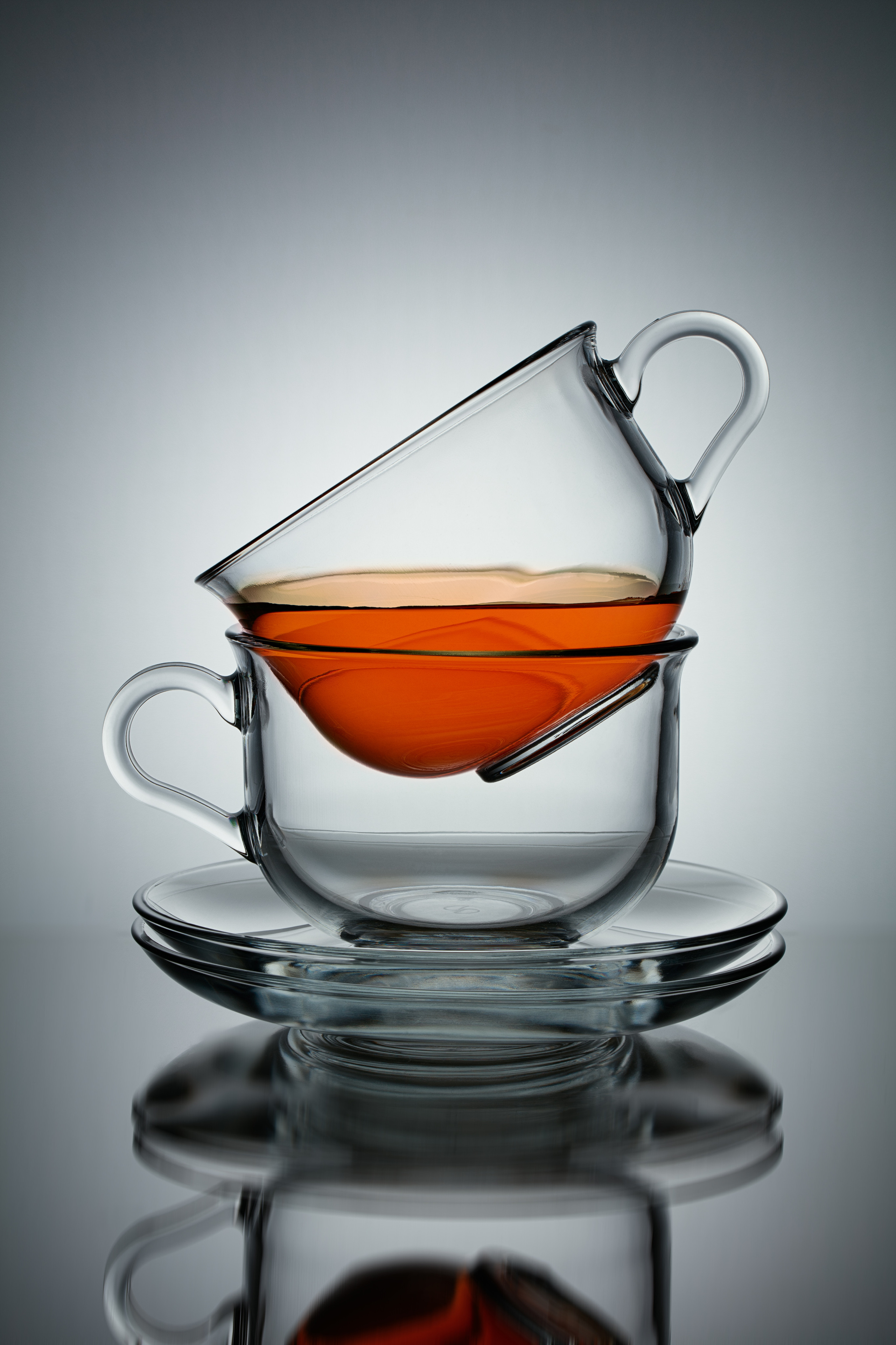 чашка с чаем под углом 45 градусов стоит на пустой которая стоит на двух блюдцах на сером радиальном градиентном фоне