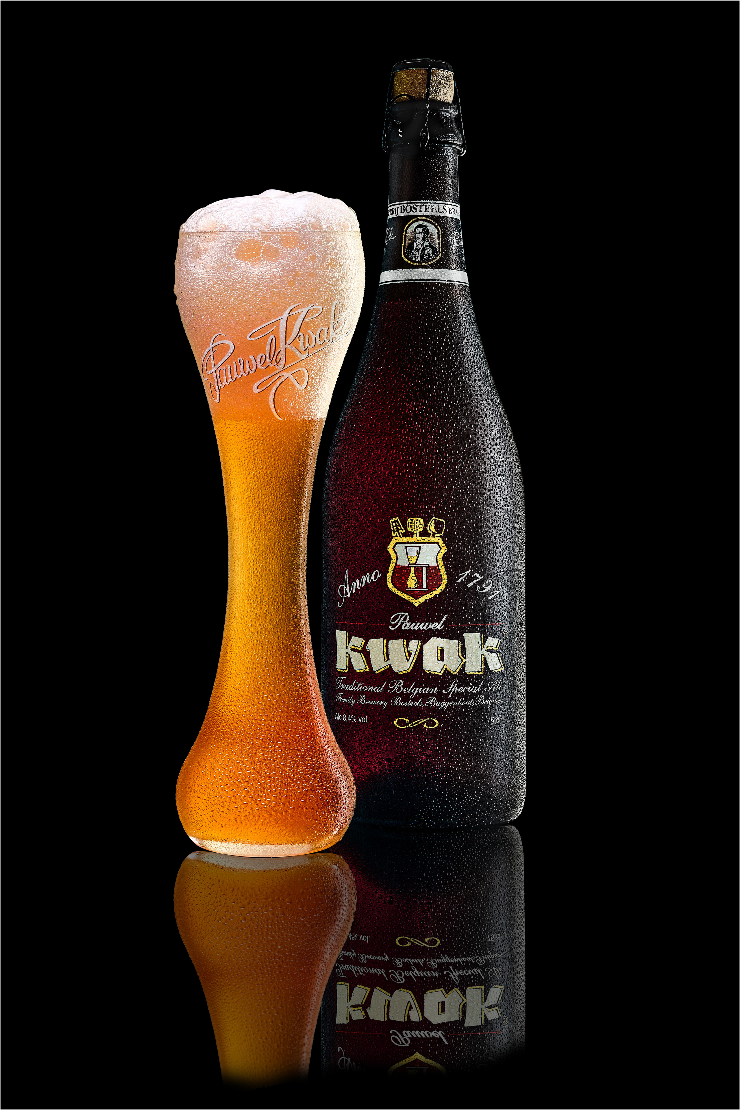  фирменный  бокал с пивом с пеной и бутылка пива Kwak на черном зеркальном столе