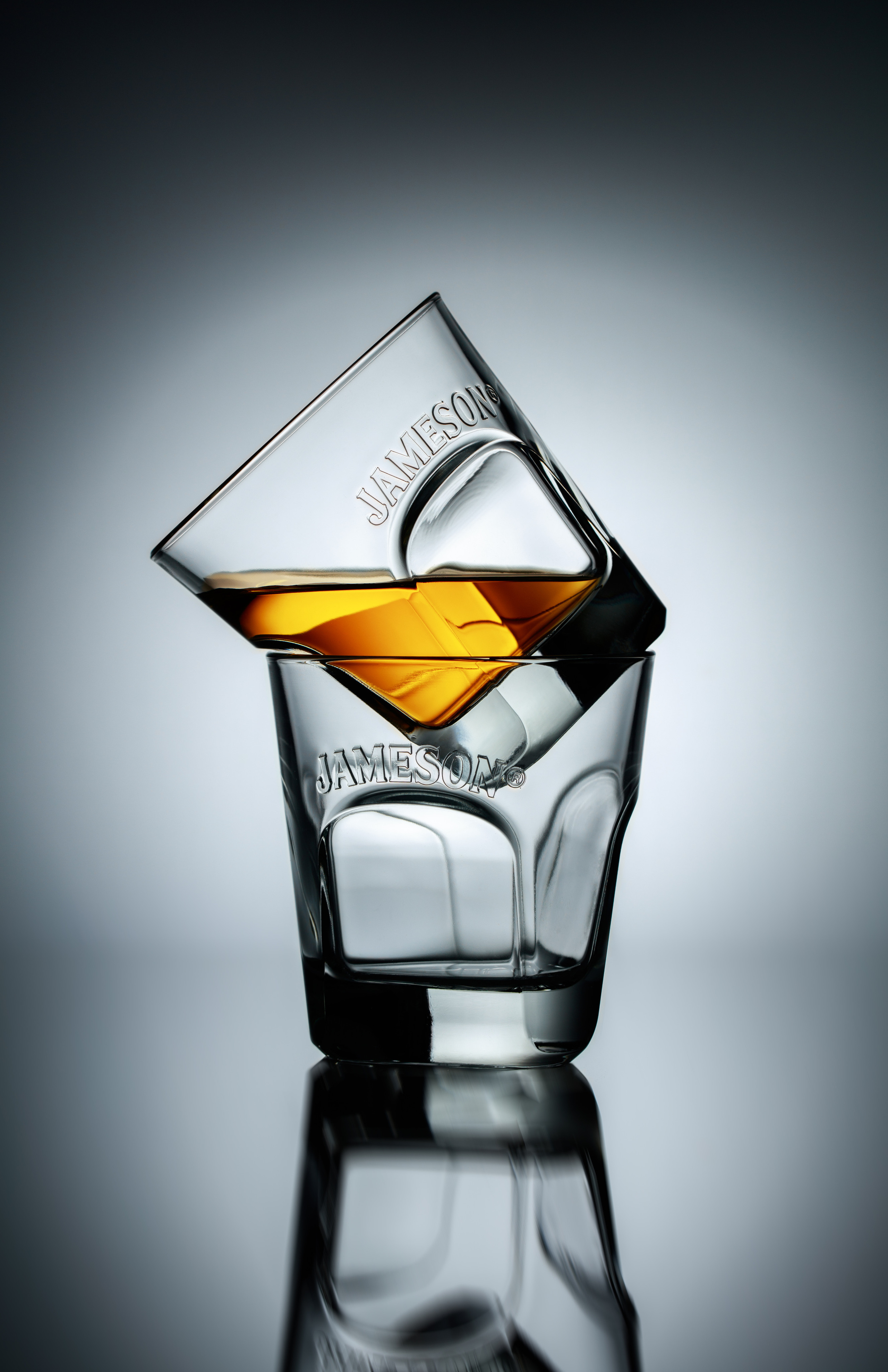 композиция из двух стаканов Jamesson-один с виски под наклоном стоит на другом на сером градиентном фоне 