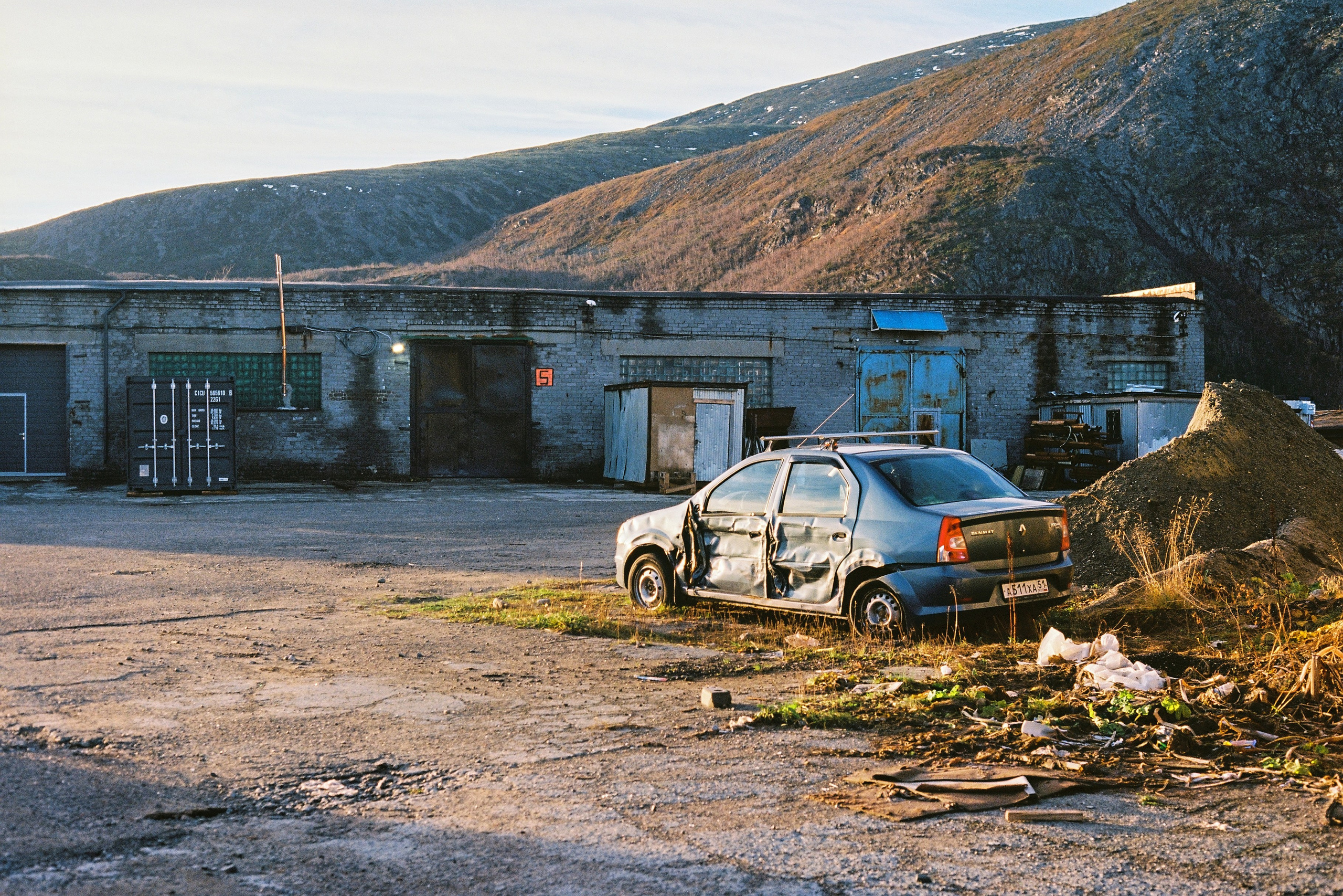 Постапокалиптичный вид на разбитую машину на фоне гаражей в Кировске