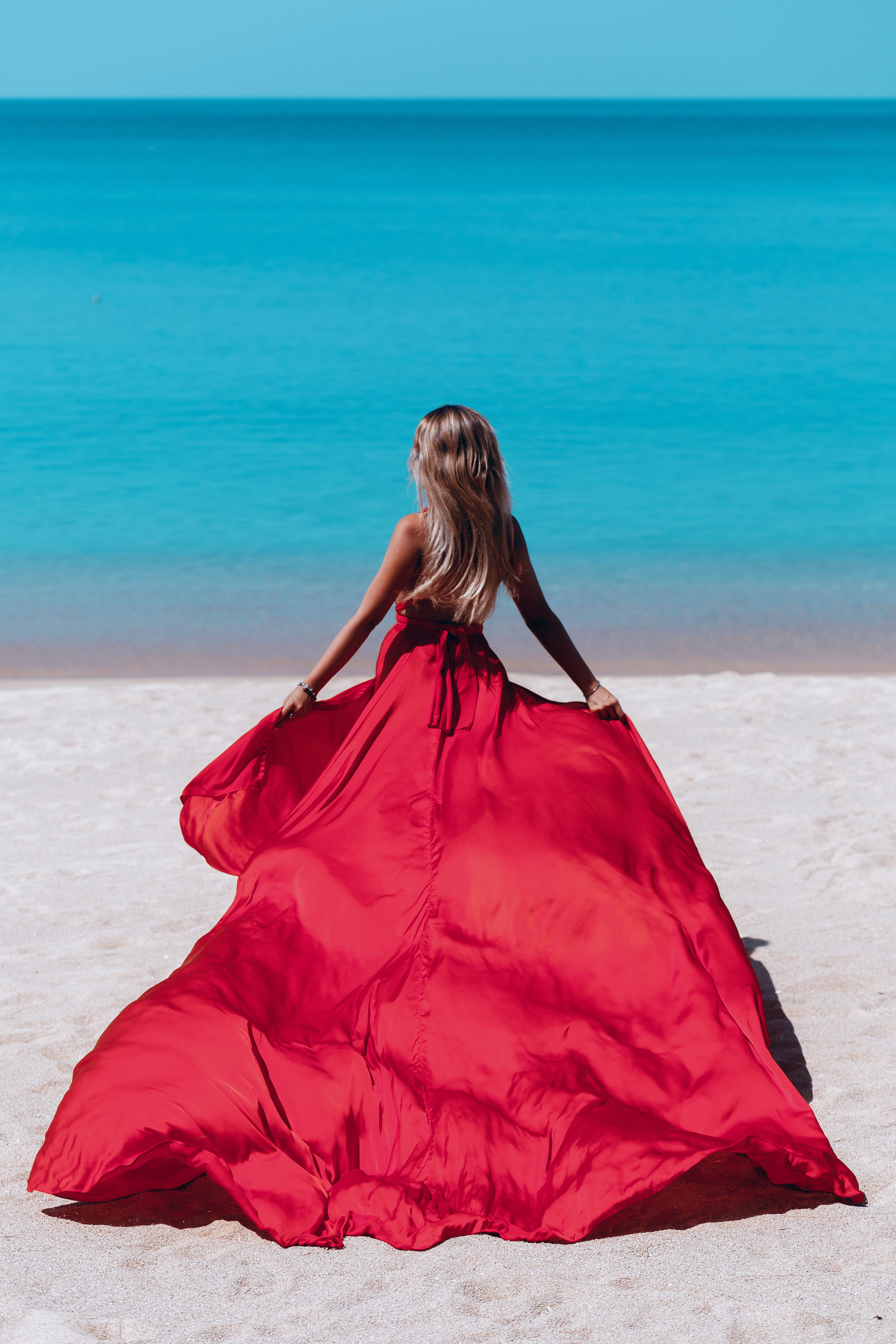 парящее красное платье на фоне бирюзового моря 