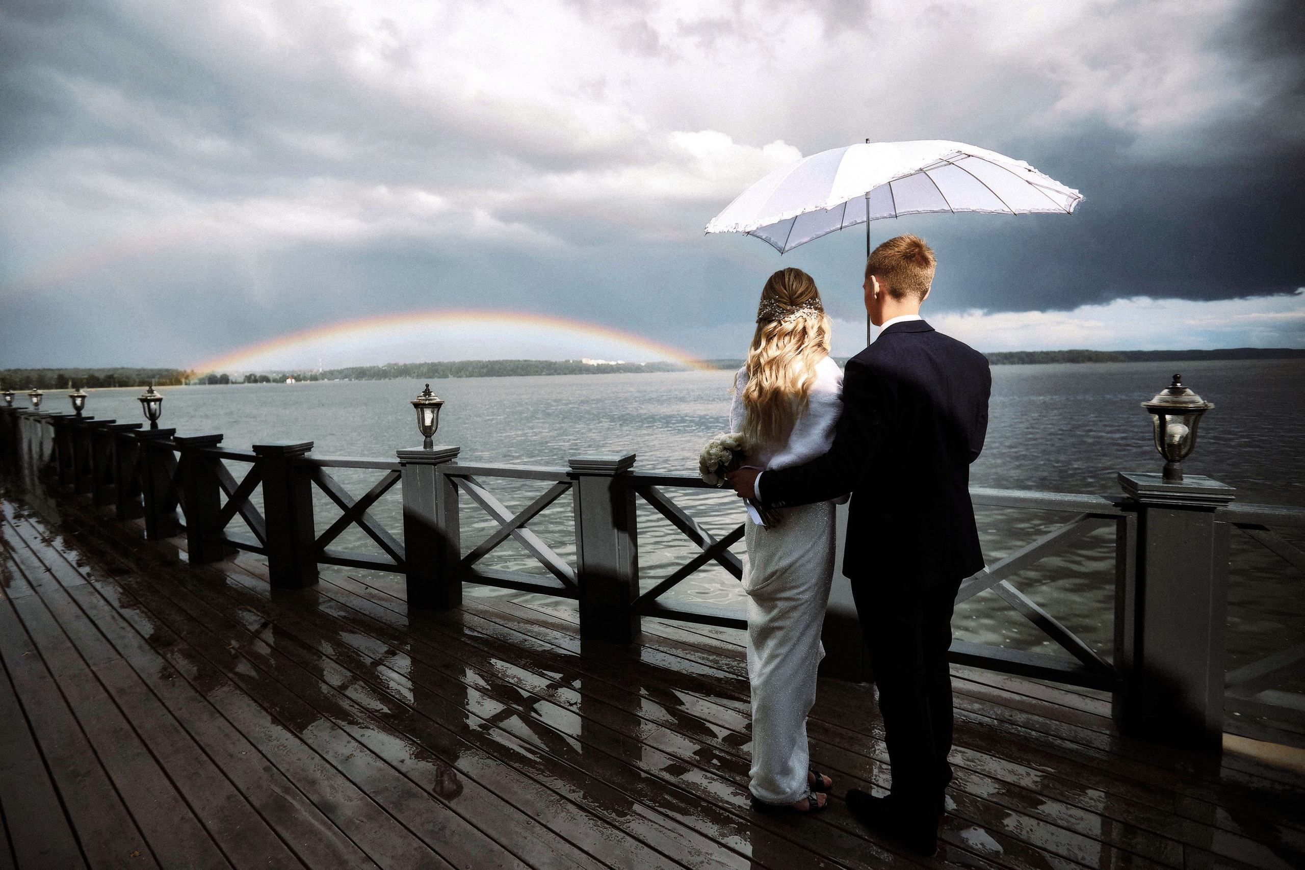 Молодожёны под зонтом на набережной, радуга над озером после дождя