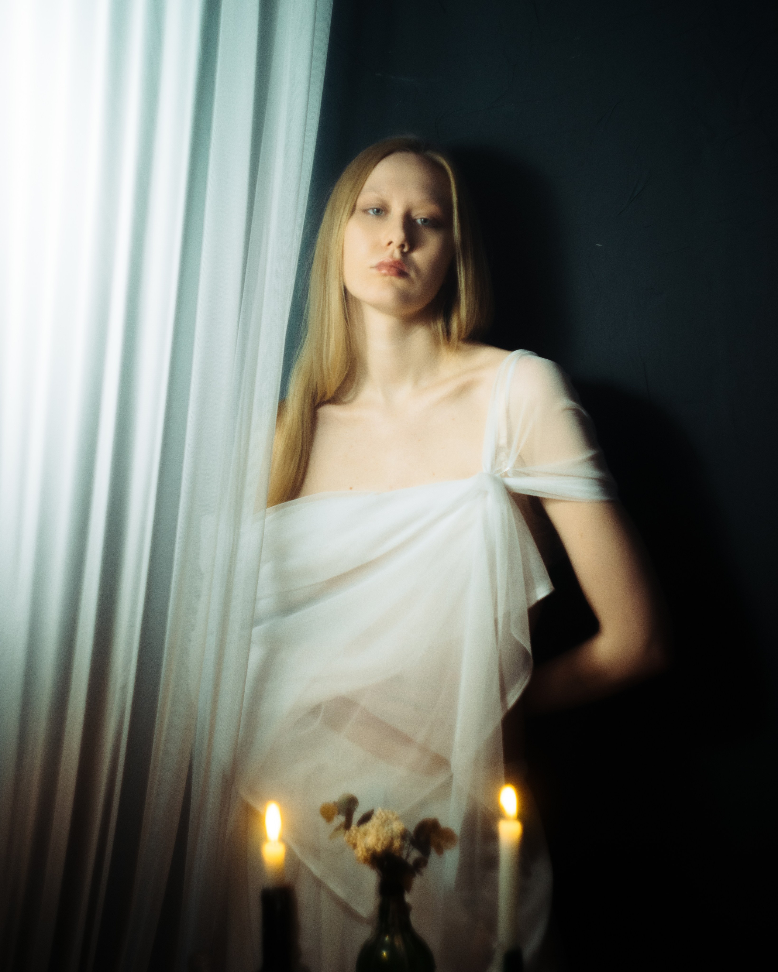 Женская фотосессия у окна со свечами, девушка в белой драпировке, авторский портрет в темной кинематографичной эстетике