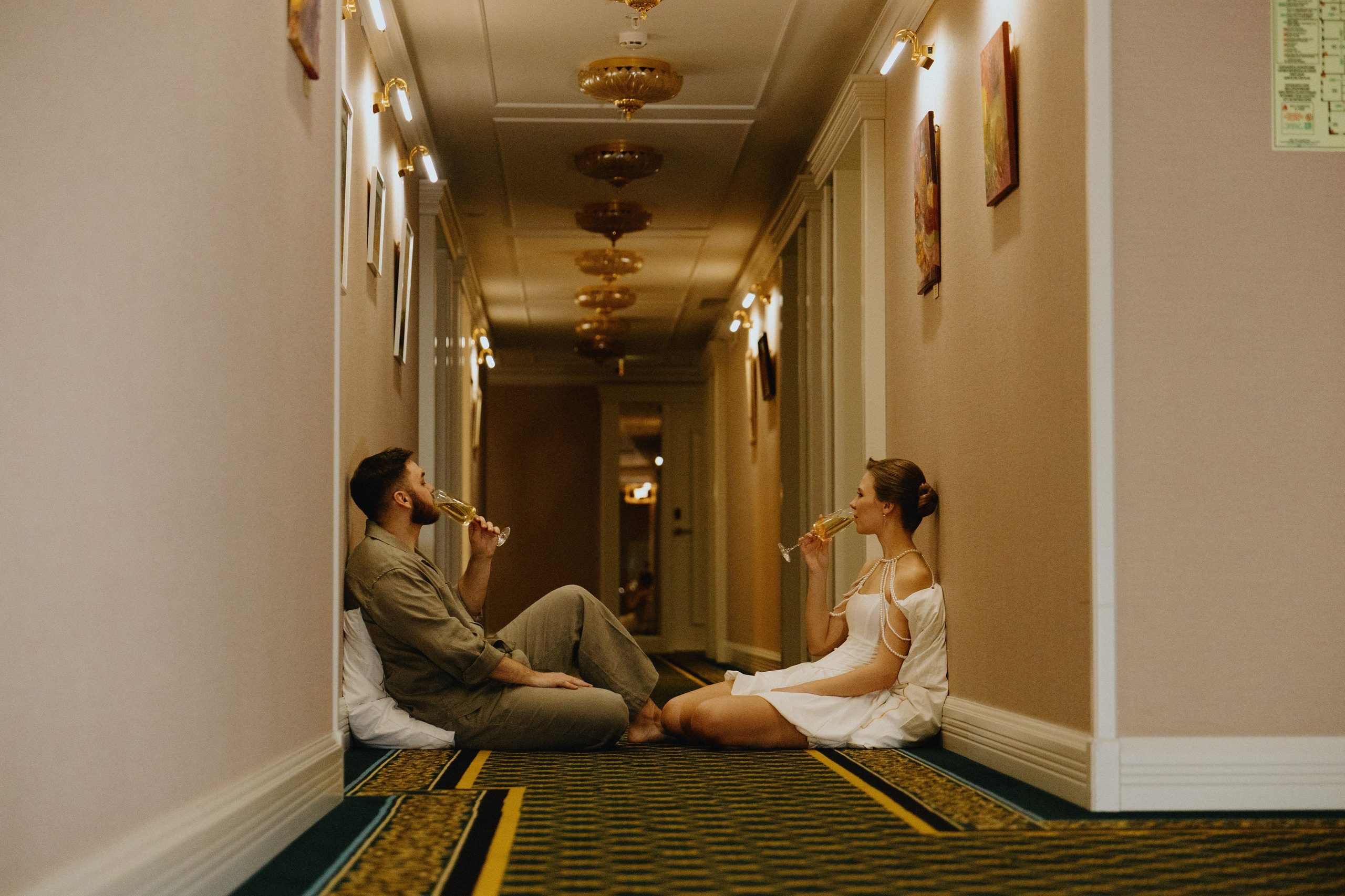 Пара пьет шампанское: Жених и невеста сидят на полу в коридоре, держа бокалы с шампанским.