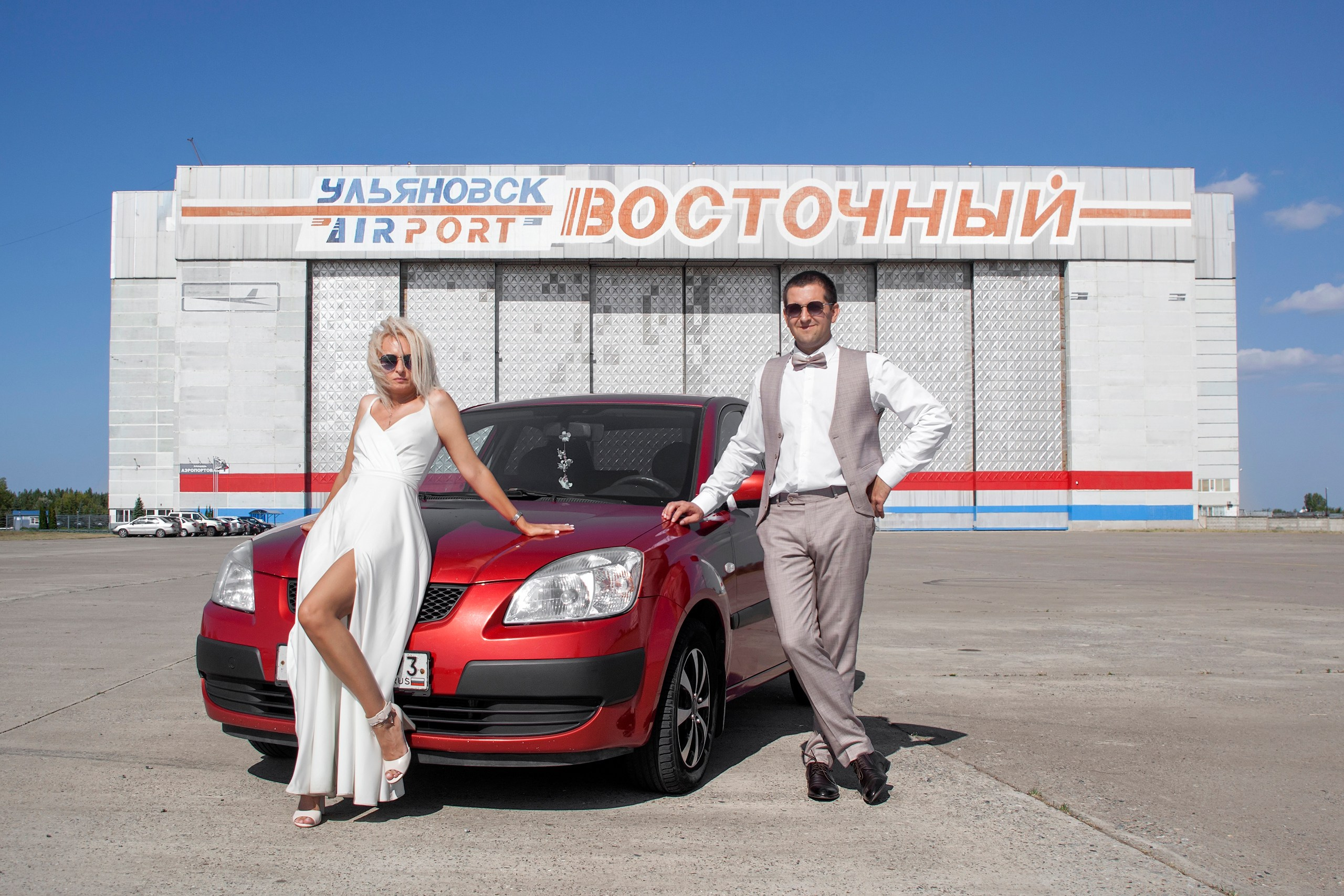 Жених с невестой около красной машины на фоне здания аэропорта Восточный - фотограф Янкаускене Наталья