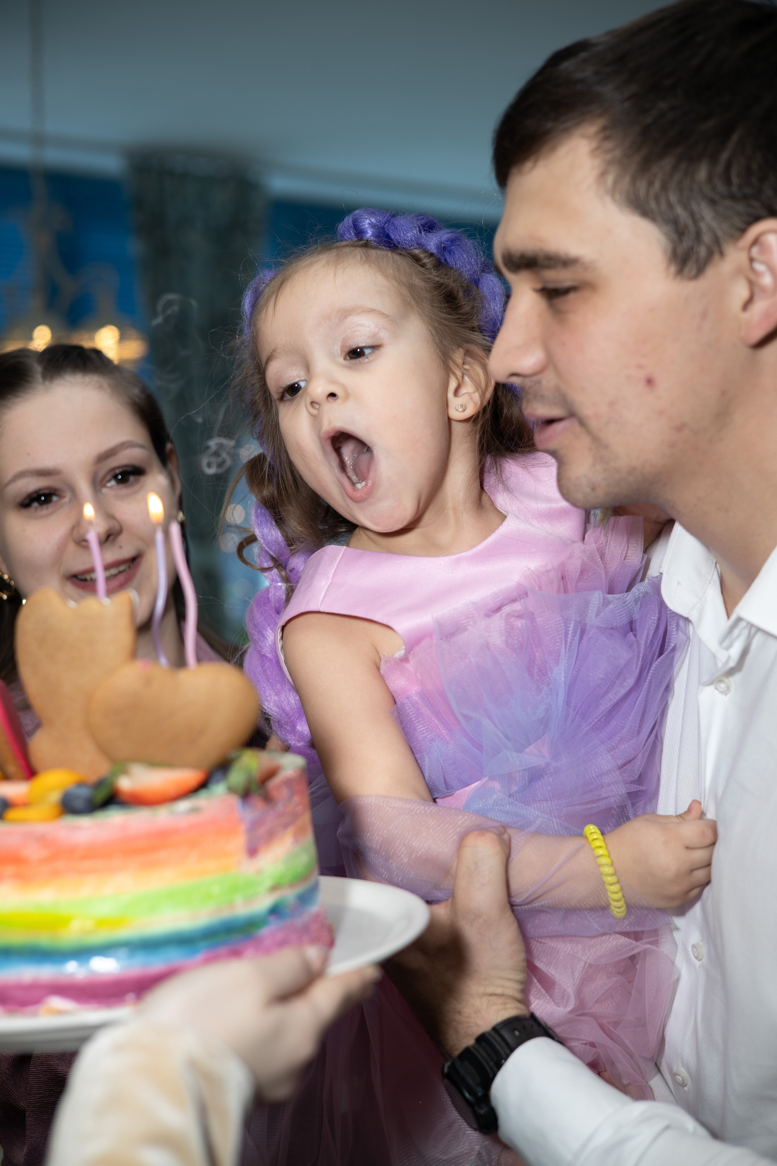 Мама, папа и дочка на руках. Дочка задувает свечи на торте. Детский день рождения  Астрахань.