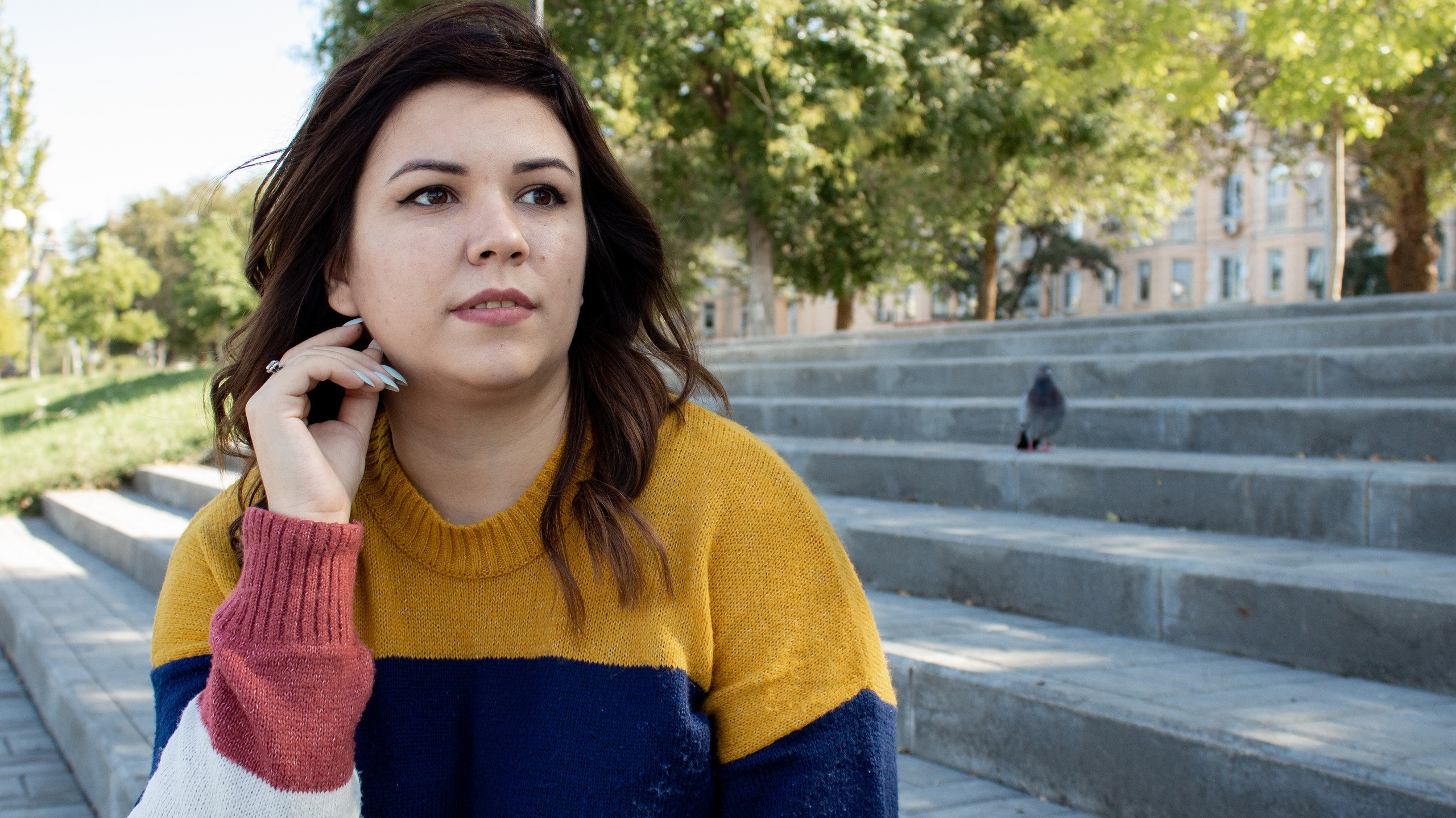 Девушка сидит на ступеньках, смотрит немного в сторону. Прогулочная съёмка.