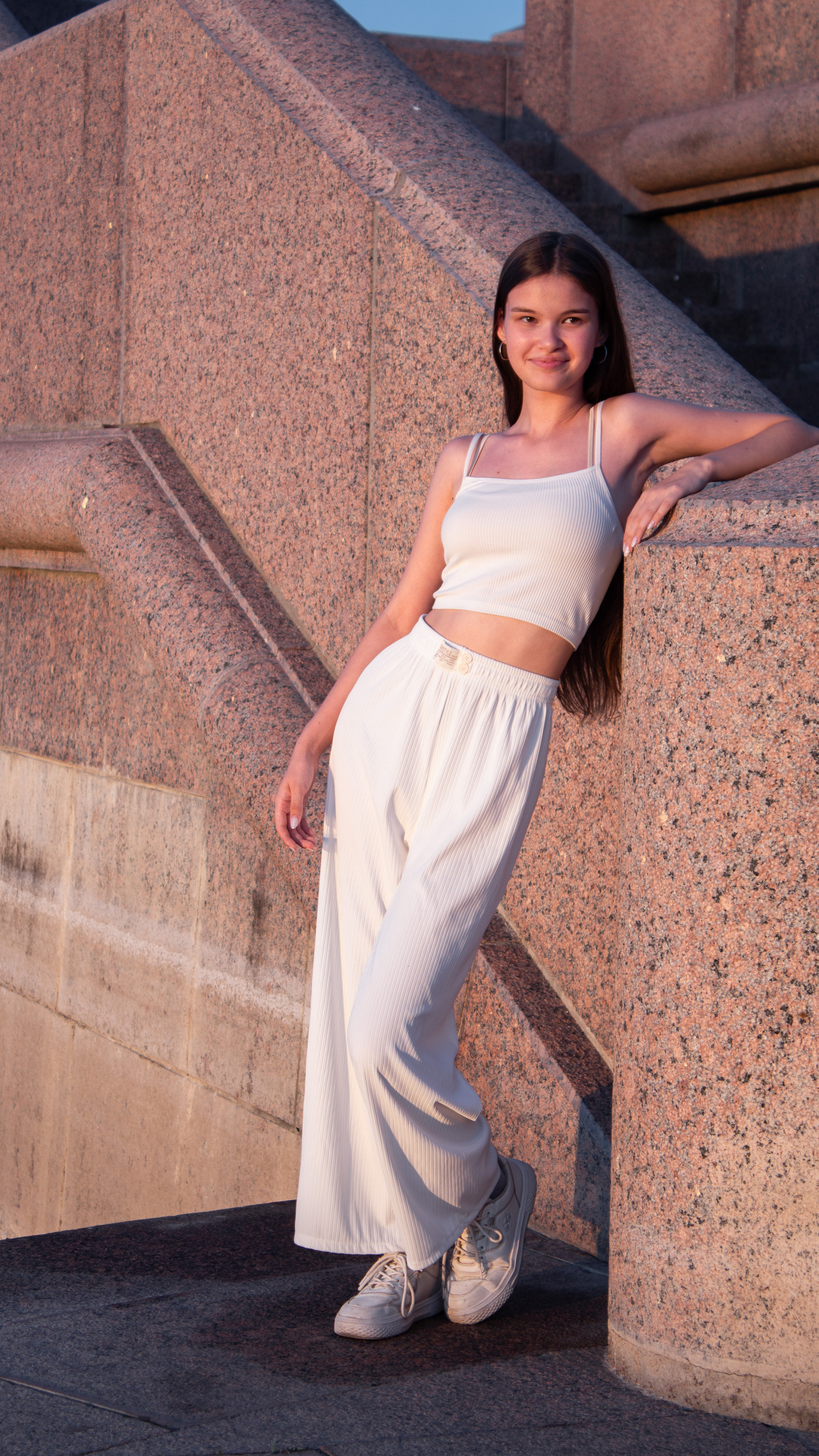 Девушка в белом костюме стоит на набережной возле гранитной стены. Прогулочная съёмка.