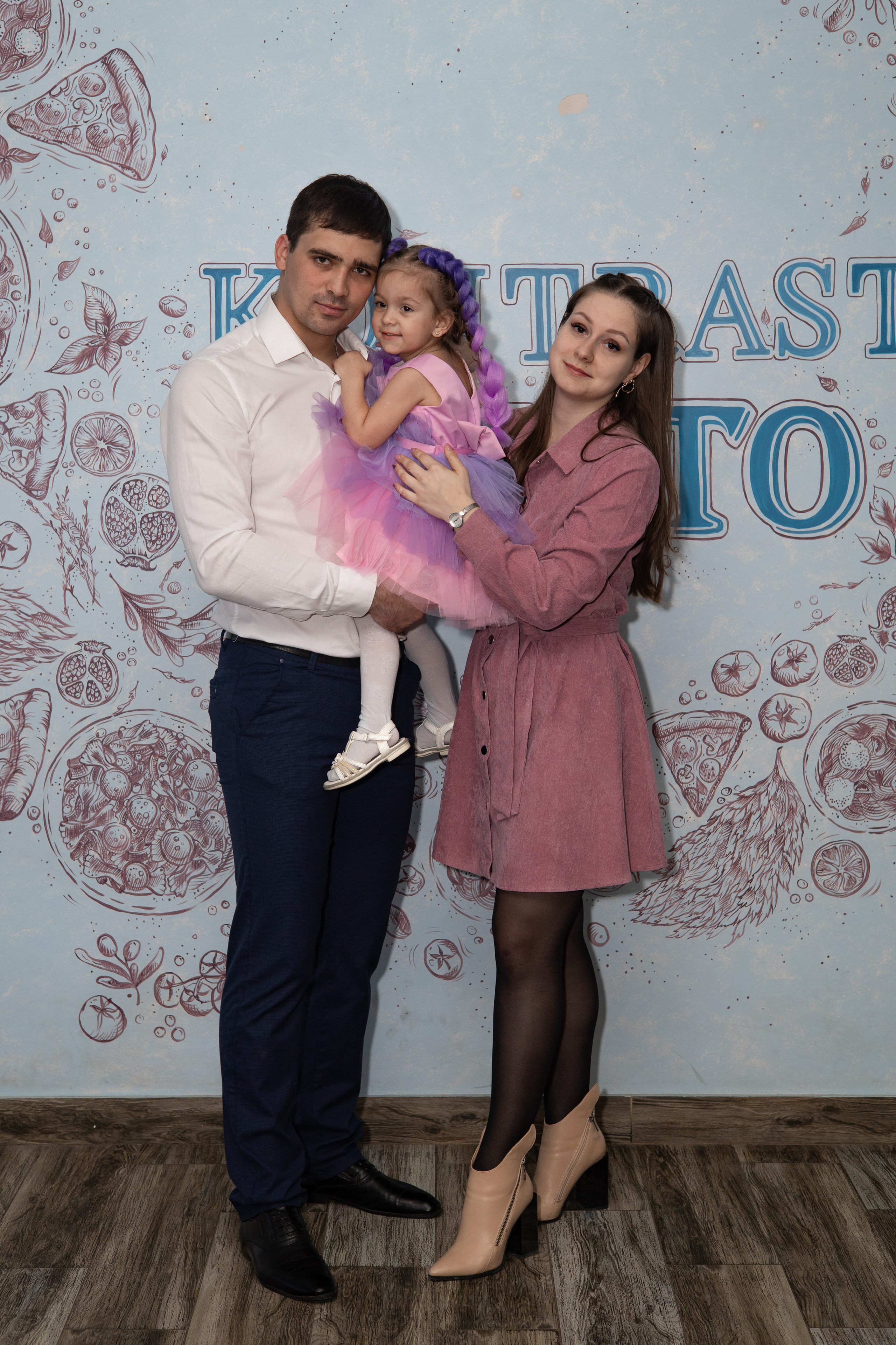 Мама, папа и дочка стоят у стены в кафе. Детский день рождения  Астрахань.