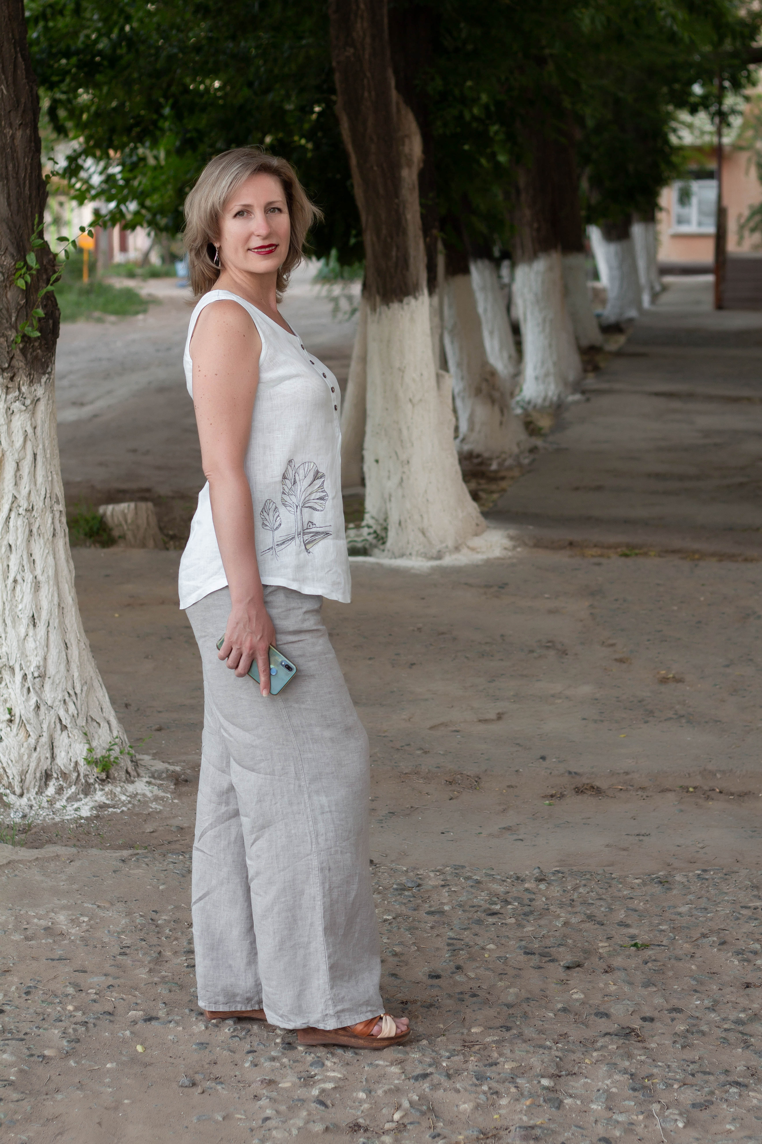 Женщина стоит на фоне аллеи, держит в руках телефон. Прогулочная съёмка.