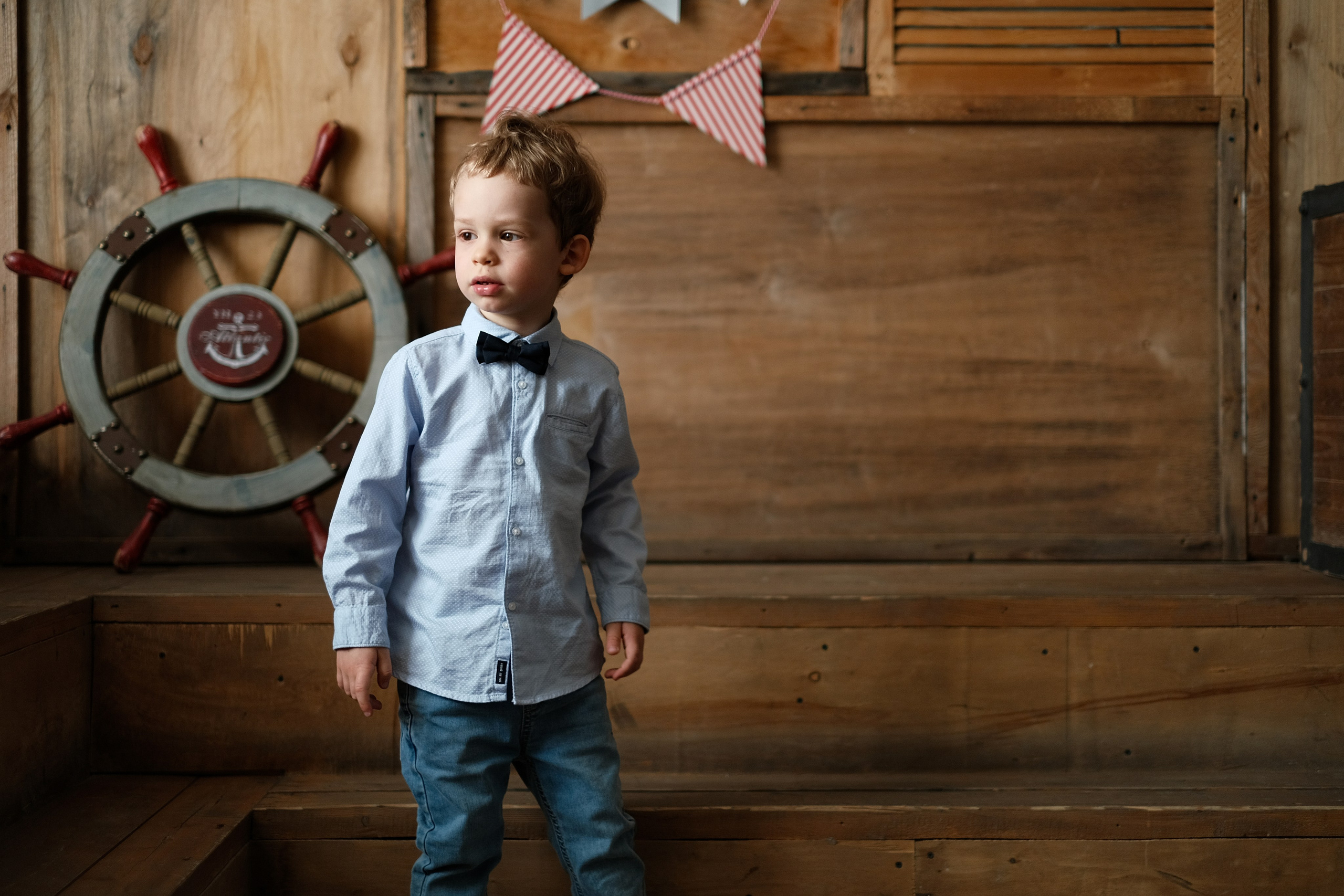 Портрет маленького мальчика в бабочке на фоне морского штурвала.