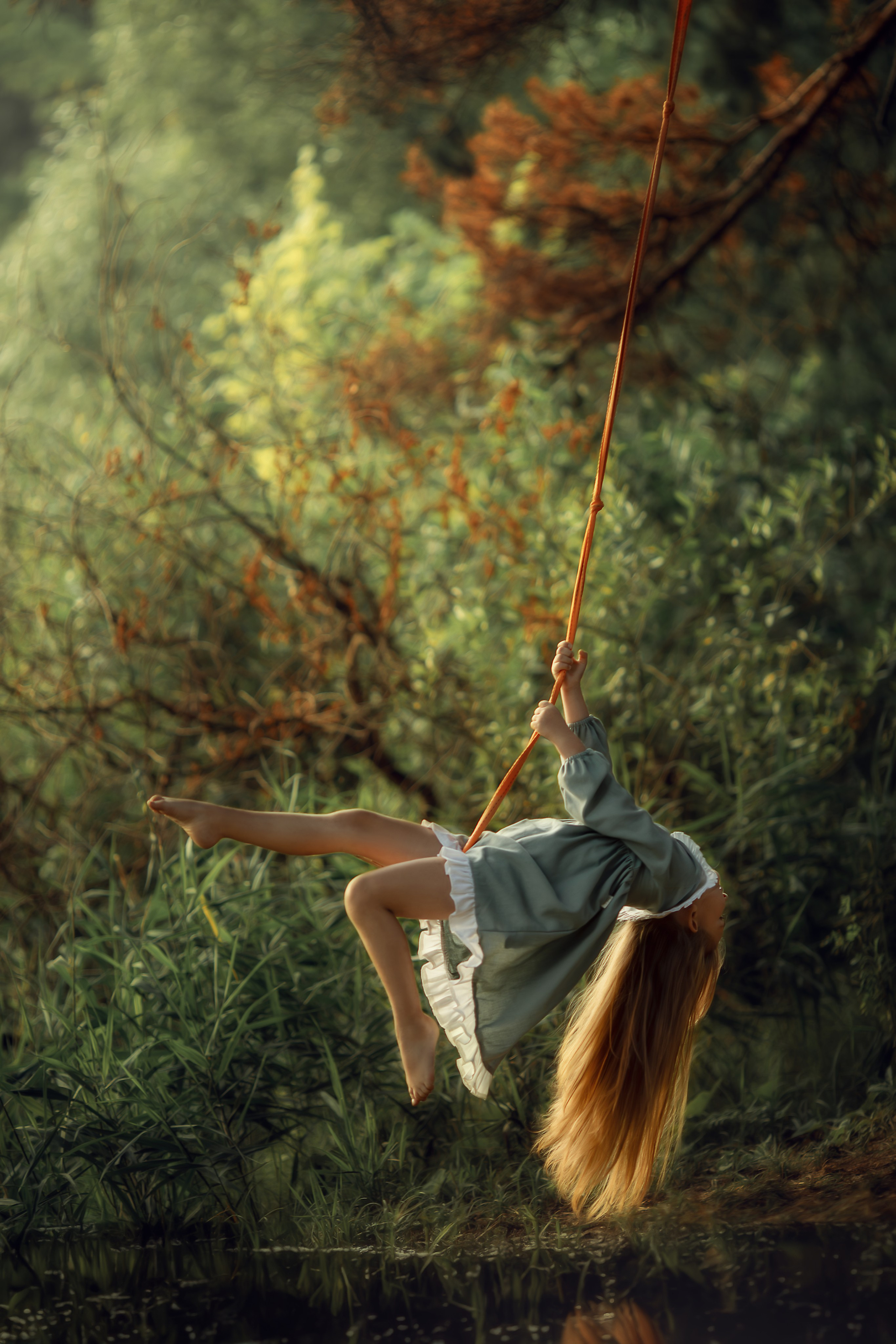 Девочка на качелях у воды, в зелёном платье с белыми рюшами