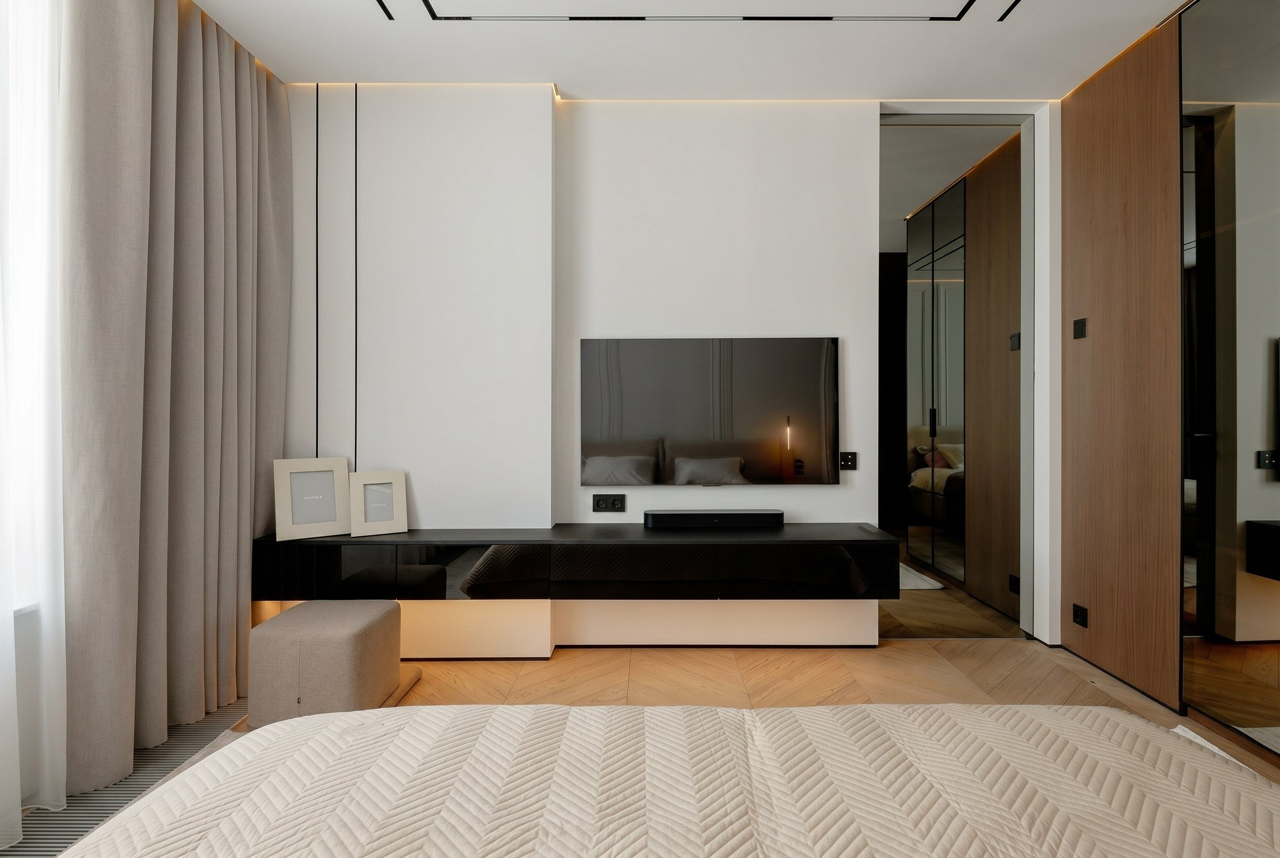 ТВ-зона в спальне квартиры 116 м² от Валерии Котович: черная подвесная тумба с подсветкой, телевизор на стене, паркет «елочка» и вход в гардеробную.