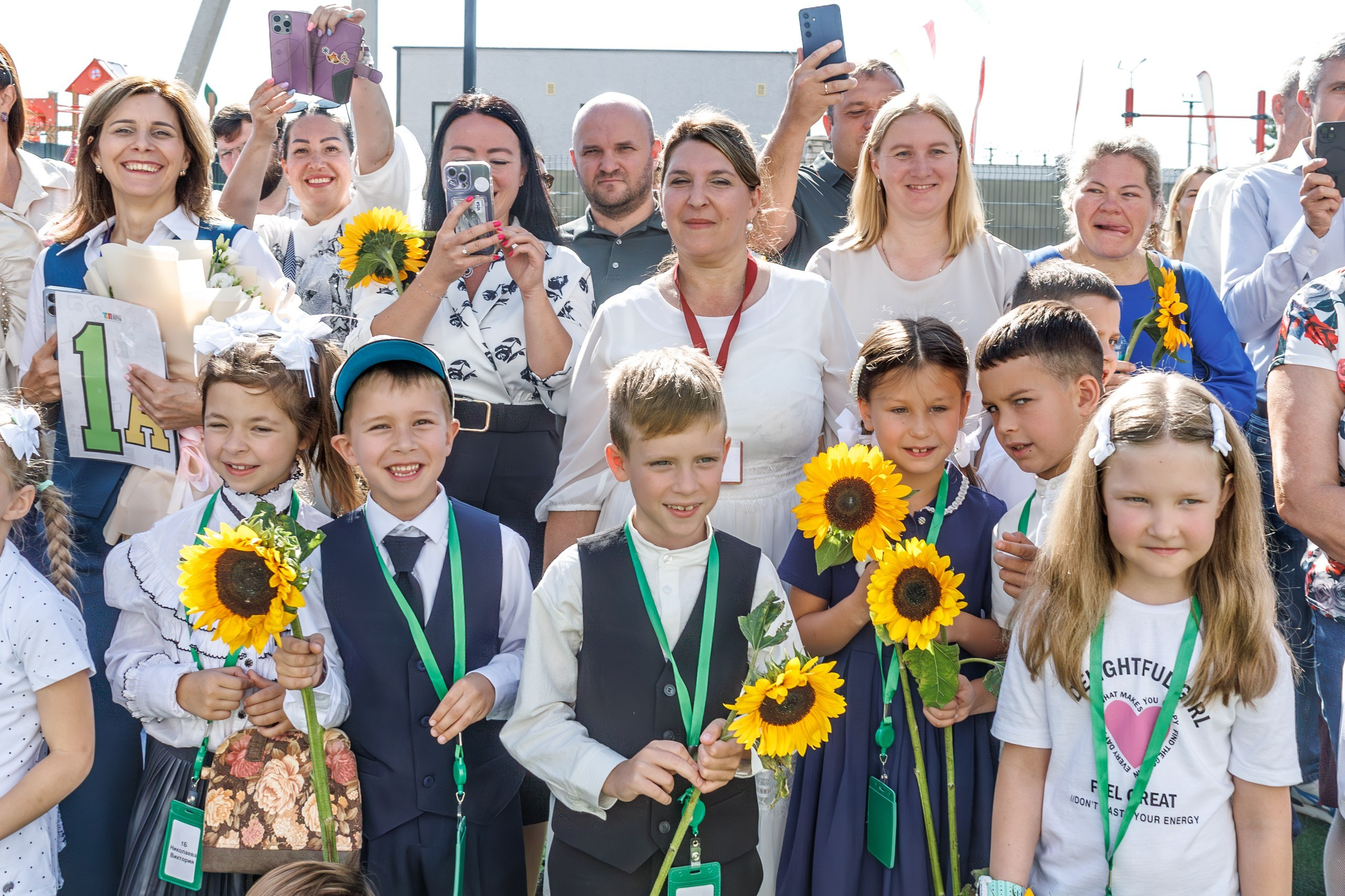 Линейка 1 сентября в школе - дети с букетами, радостные родители и учителя; дети обнимаются, радуются встрече с друзьями после каникул