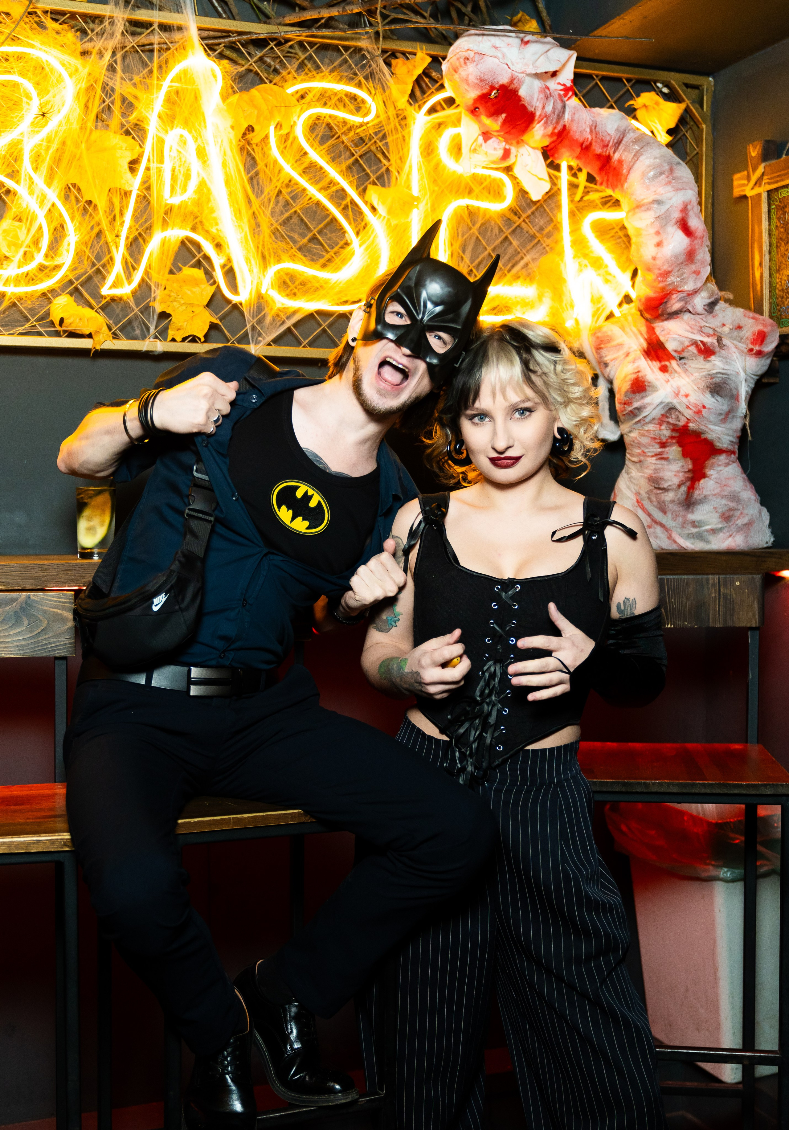 Гость в костюме Бэтмена и девушка в черном наряде позируют у Halloween‑декорации бара Debaser, Санкт‑Петербург. Репортажные фотографии Хэллоуина 2025 от Евгения Мальцева, костюмы и праздник в кадре.