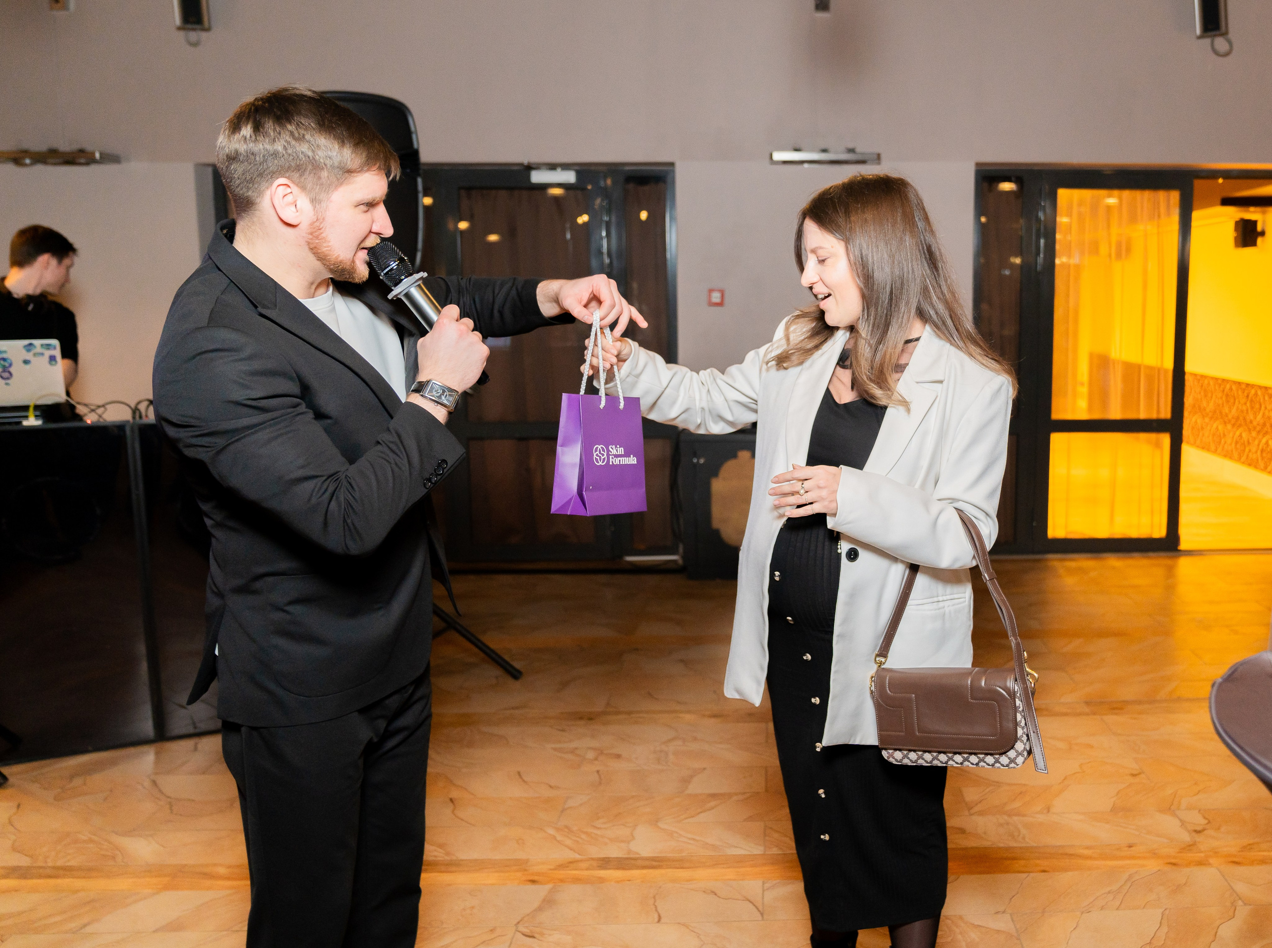 Ведущий вручает победительнице фиолетовый подарочный пакет Skin Formula на розыгрыше в Radisson Sonya. Беременная девушка улыбается. Фото Евгения Мальцева (evrednix.ru).