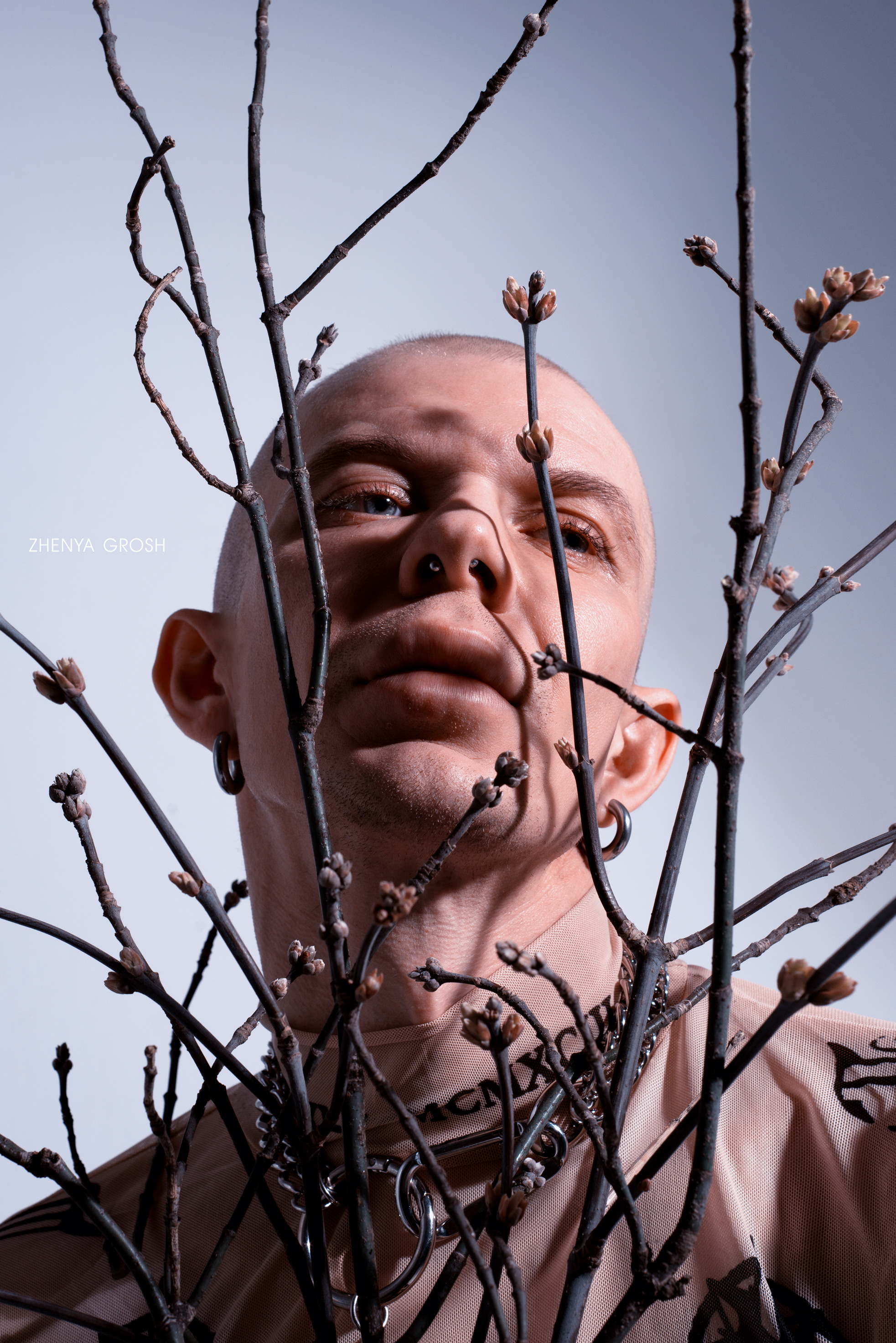 лысый мужчина в татуировках держит ветки перед лицом 