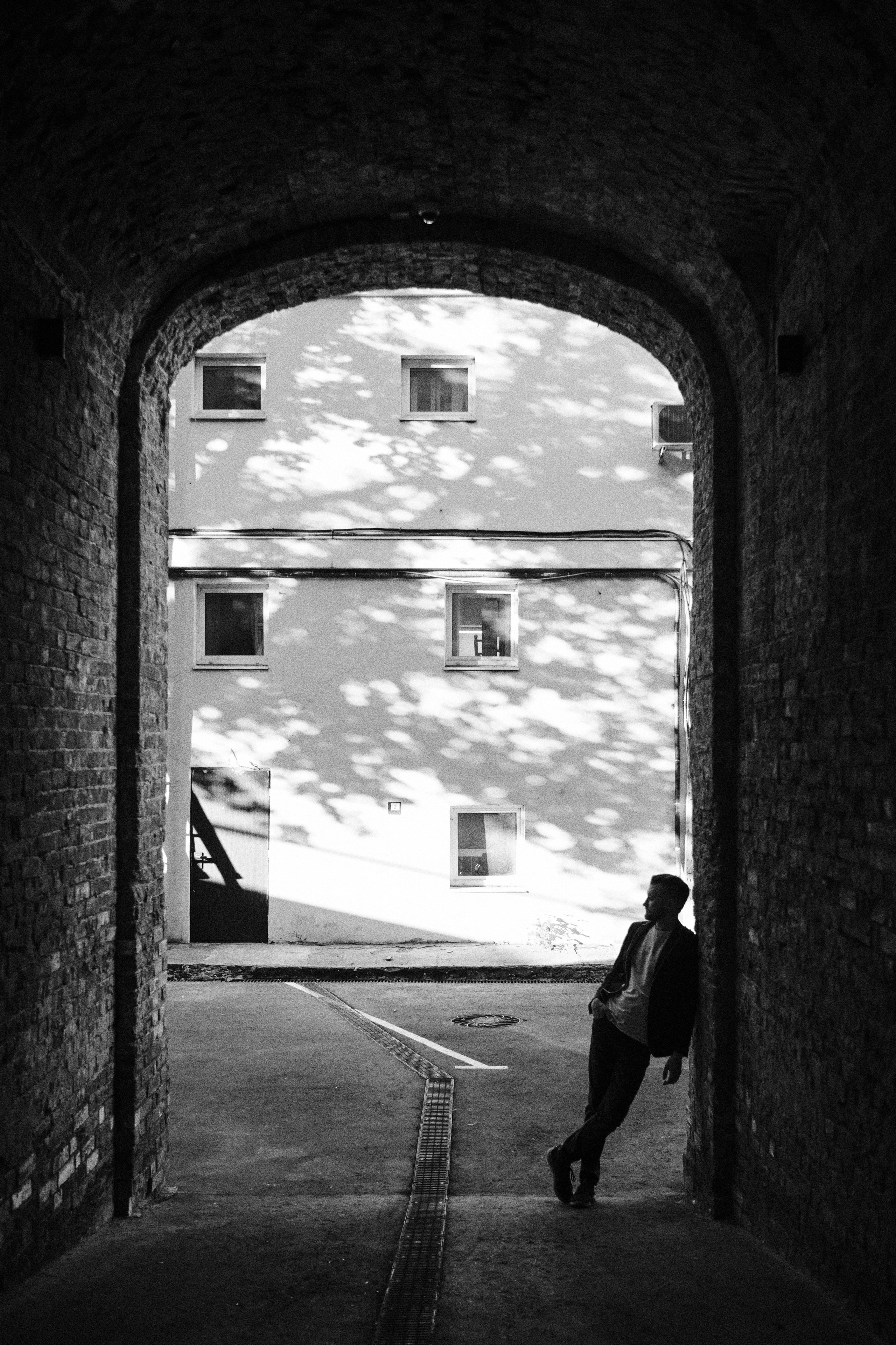 Мужчина стоит облокатившись о стену в арке старого дома