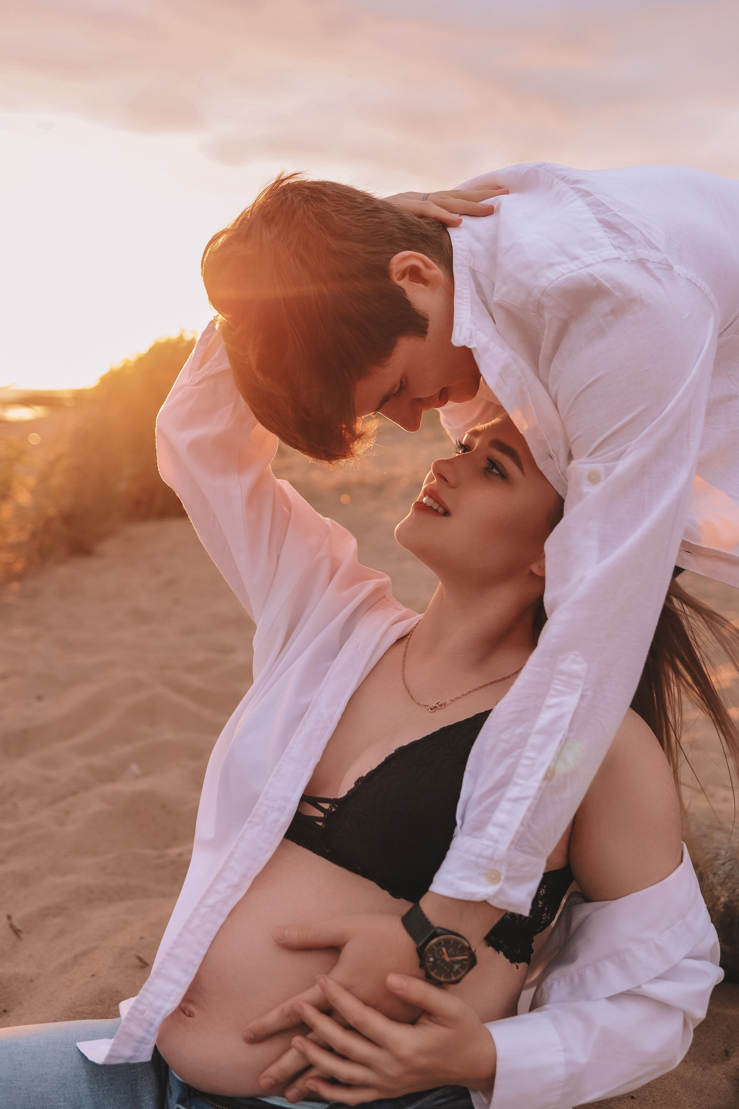 Пара обнимается, сидя на песке, закат