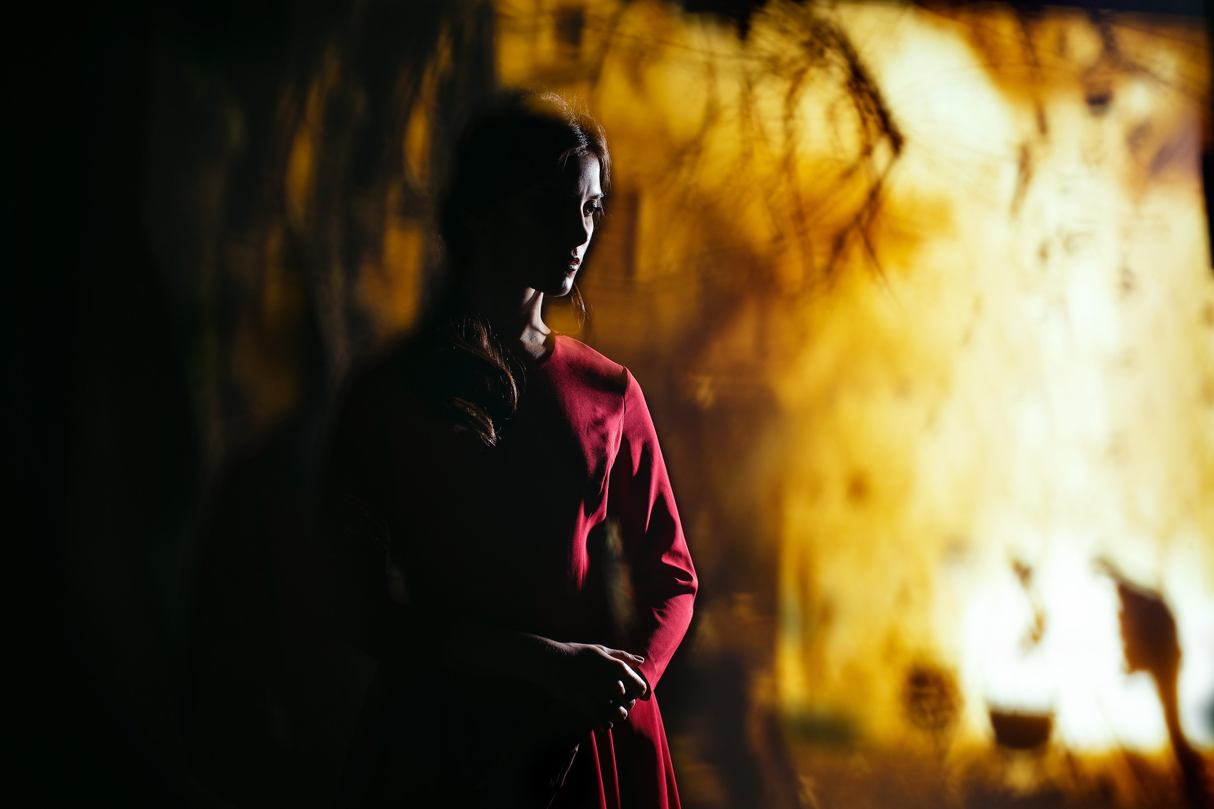 девушка в красном платье  стоит печальная на фоне огня