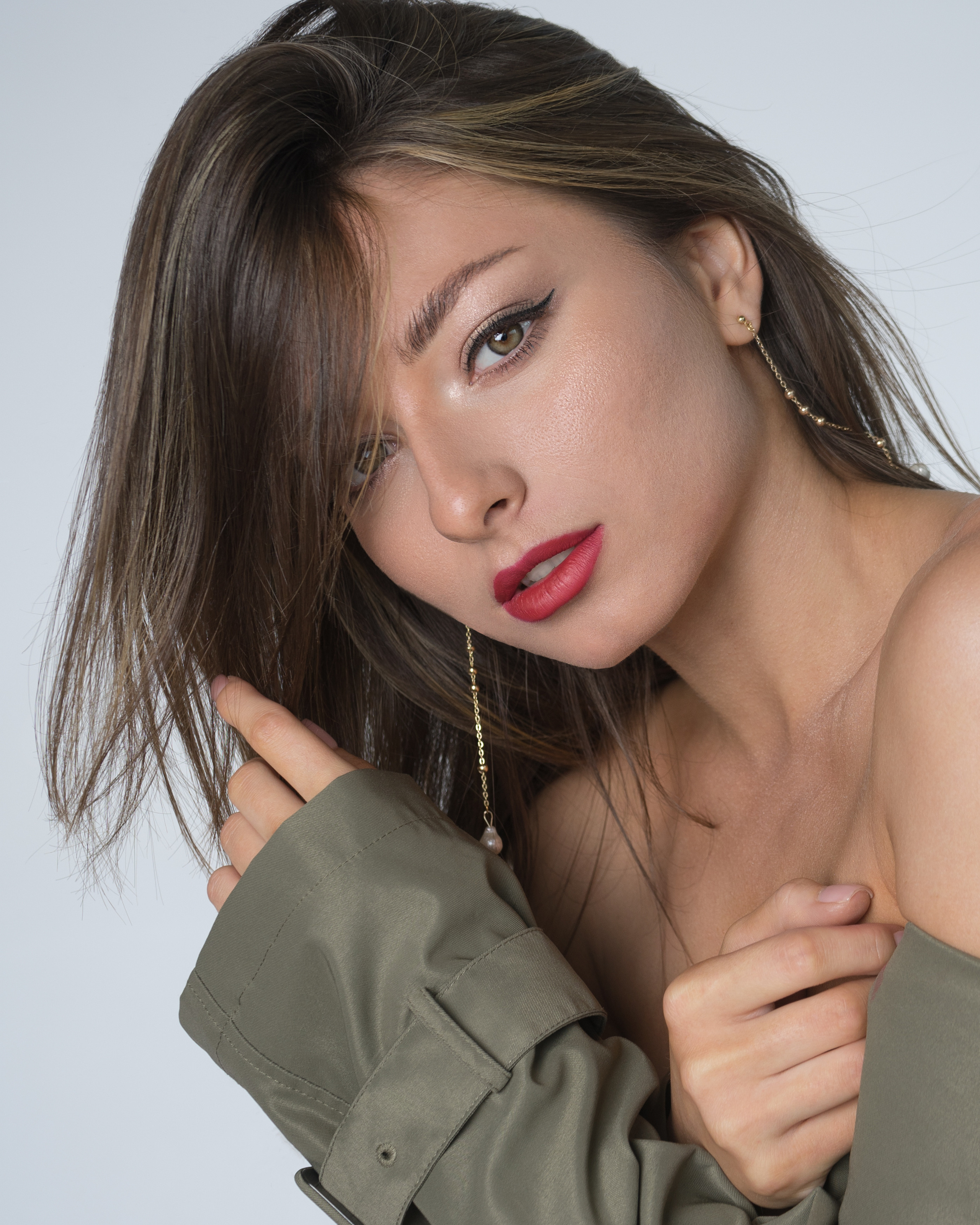 Красивая молодая девушка с тёмными волосами с красной губной помадой на губах в тренче цвета хаки