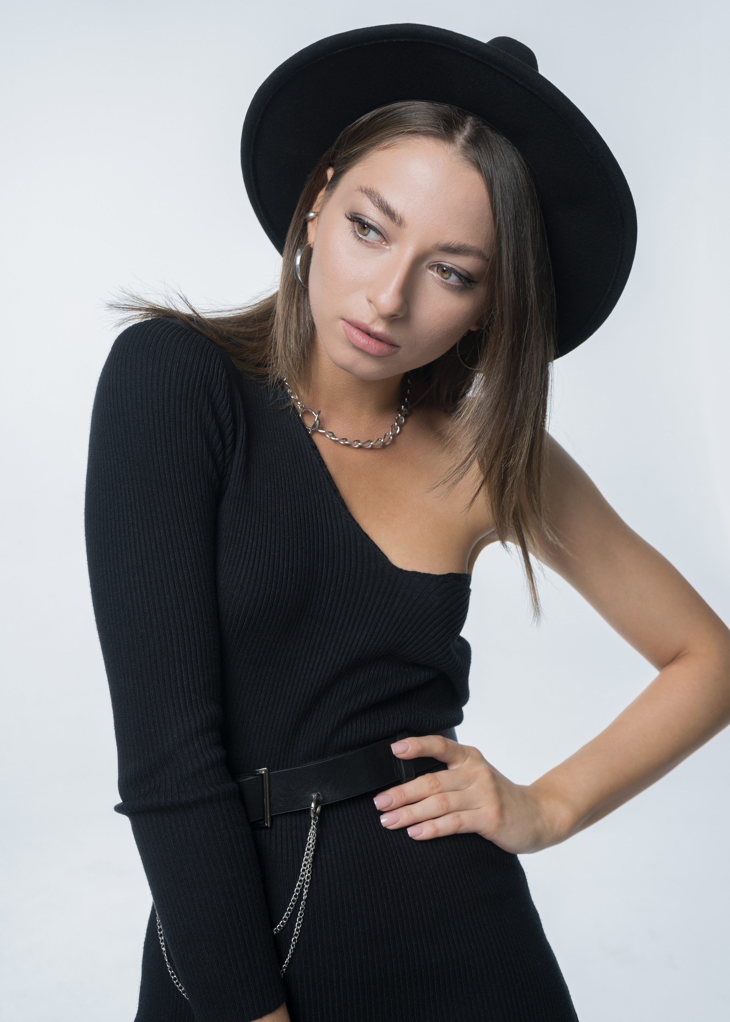 Красивая молодая девушка с тёмными волосами в черном платье с оголённым плечом и фетровой шляпе