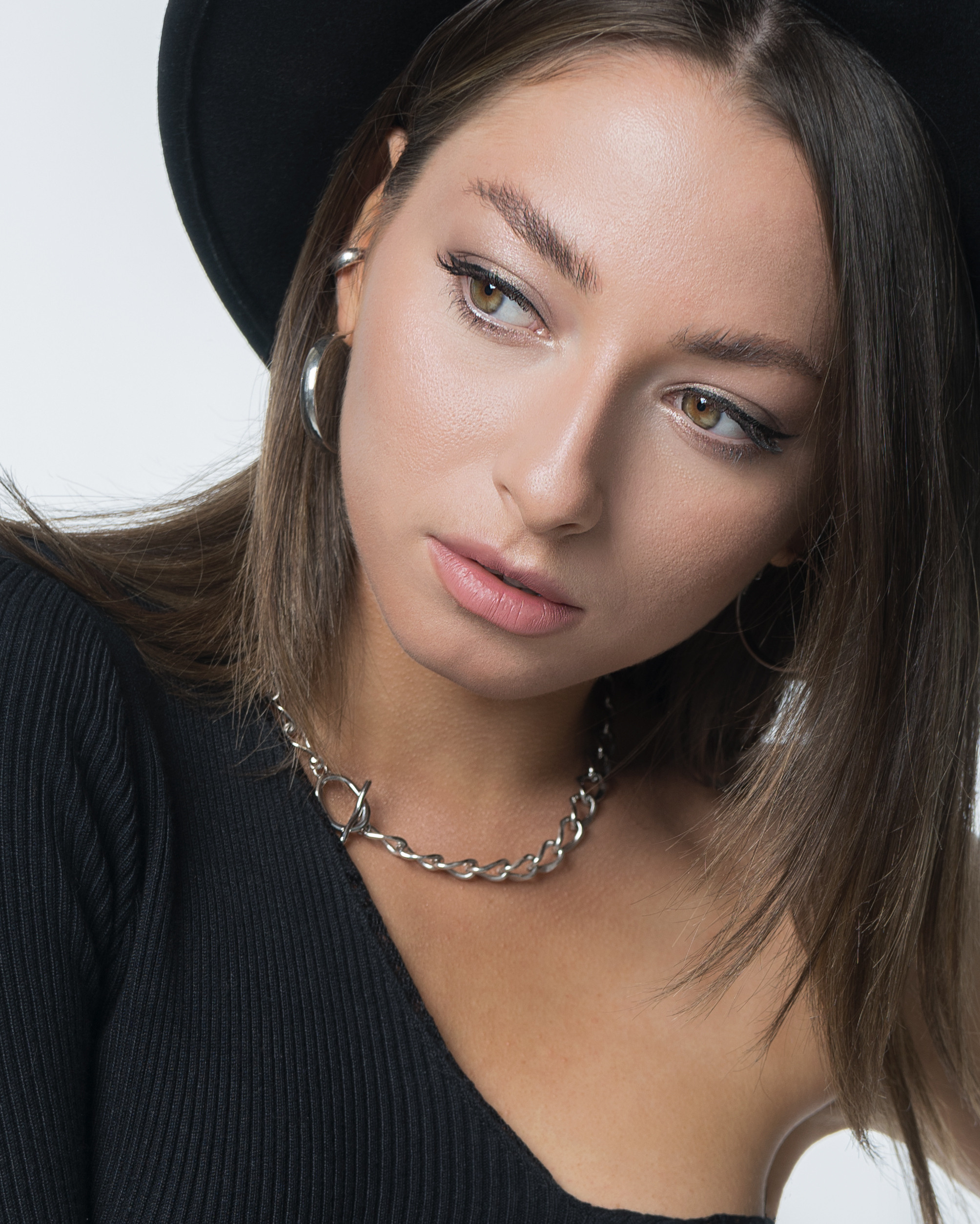 Красивая молодая девушка с тёмными волосами в черном платье с оголённым плечом и фетровой шляпе кадрирование портрет