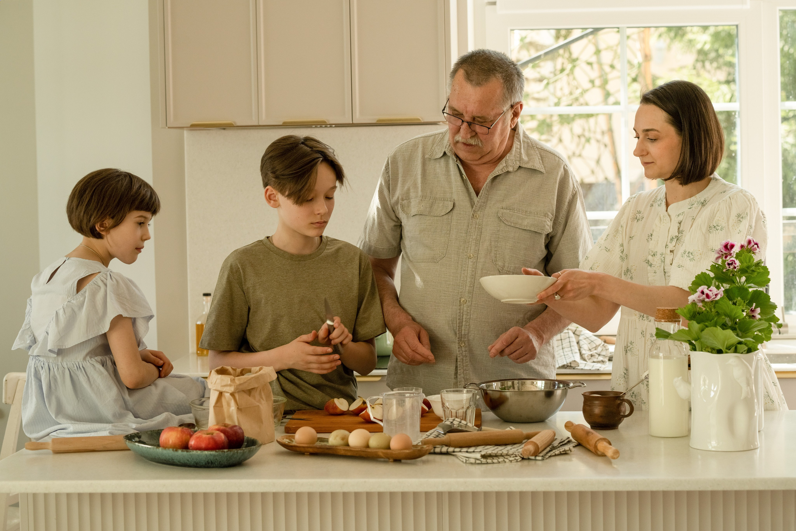 Внуки или дети готовят еду с дедушкой на кухонном острове.