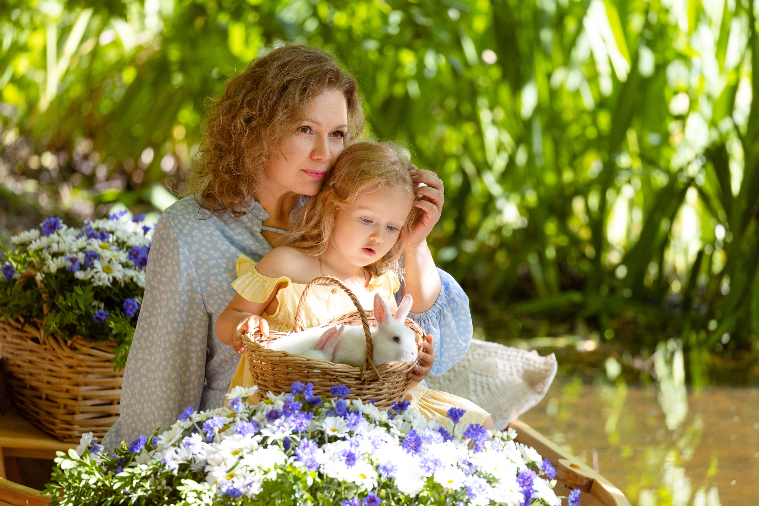 Мама с дочерью в лодке с цветами гладят Белых пушистых кроликов