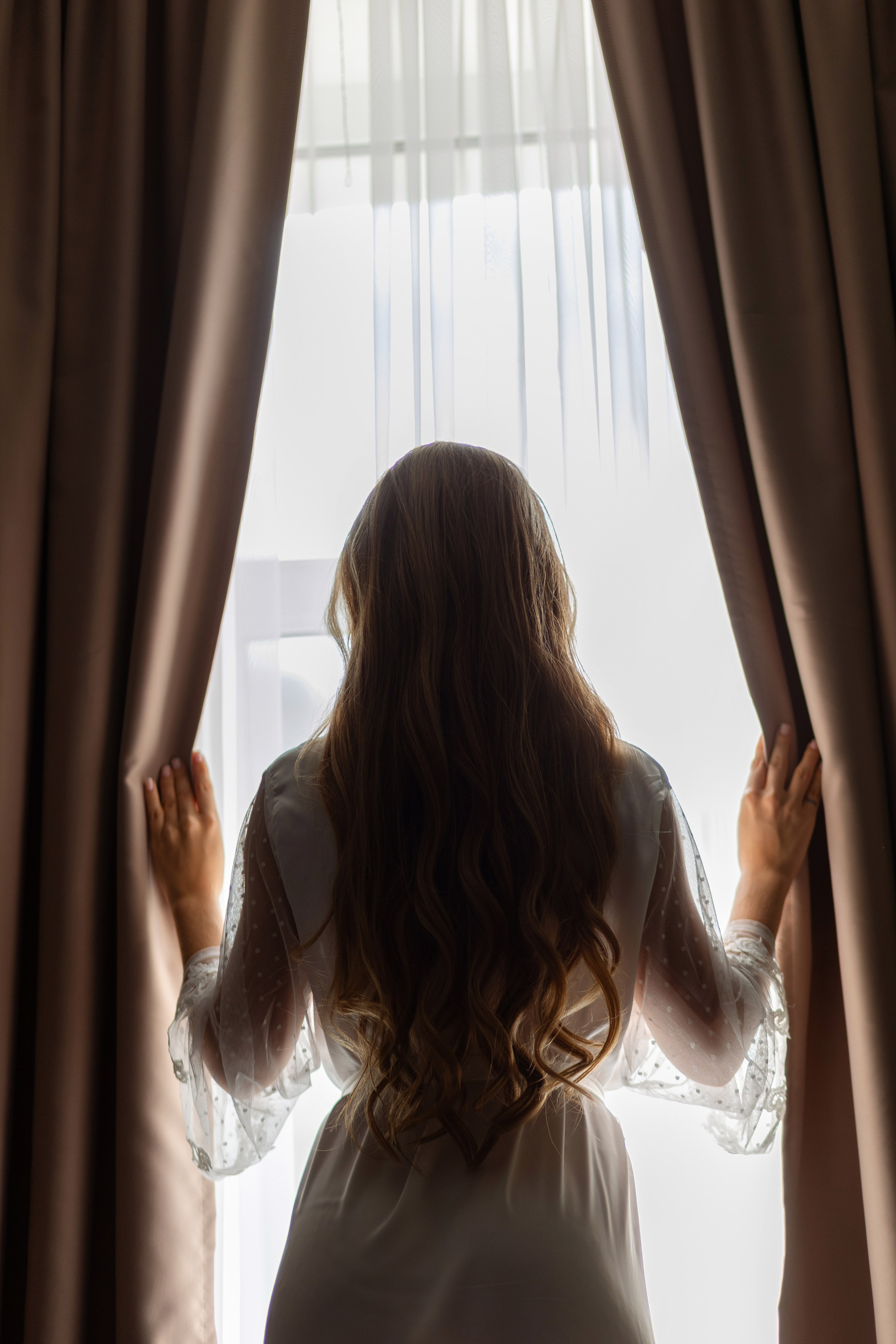 Невеста стоит у окна и раздвигает шторы.