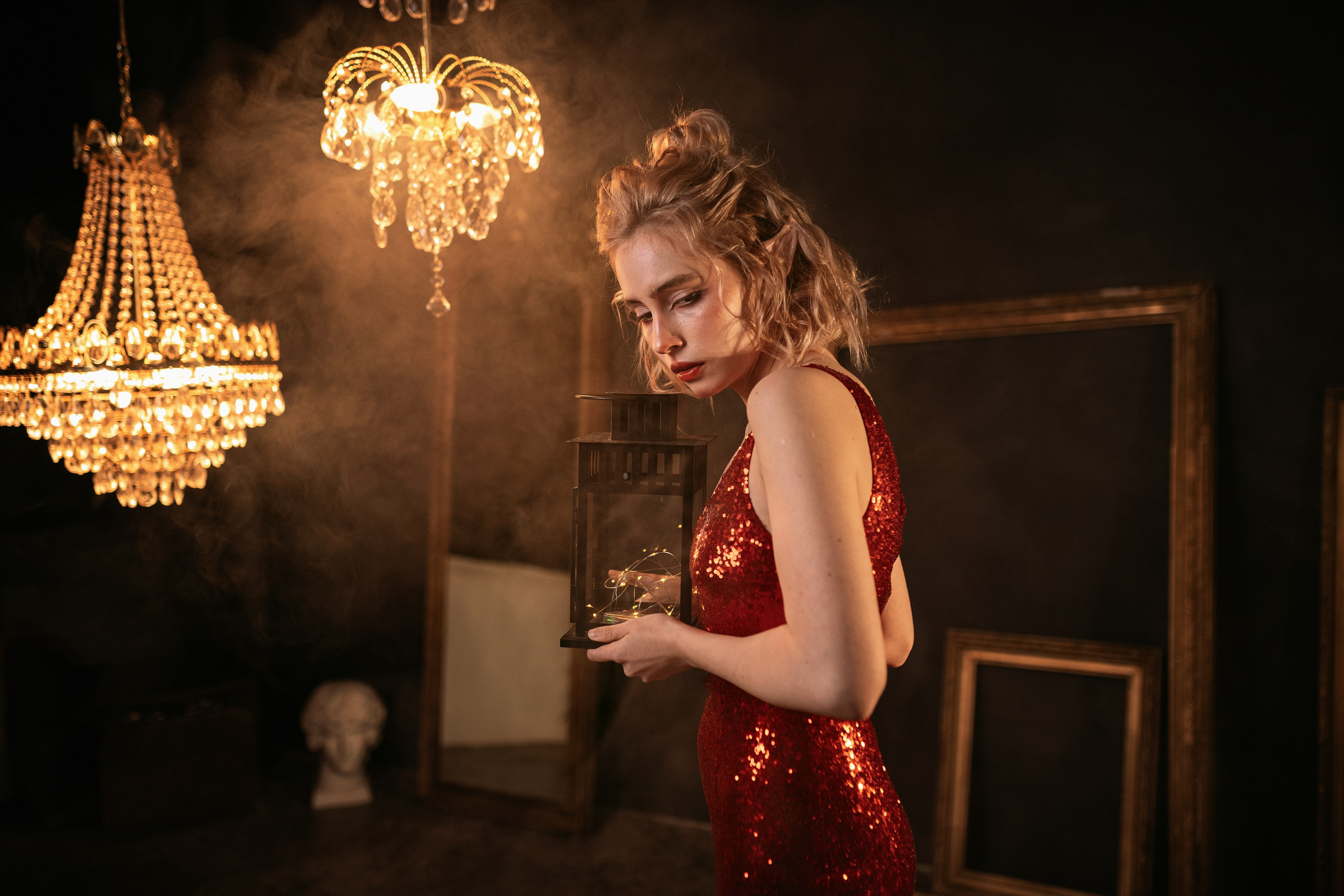 В мягко освещенной комнате, украшенной винтажным декором, женщина в красном платье с блестками держит фонарь, излучая таинственное очарование и привлекательную внешность.