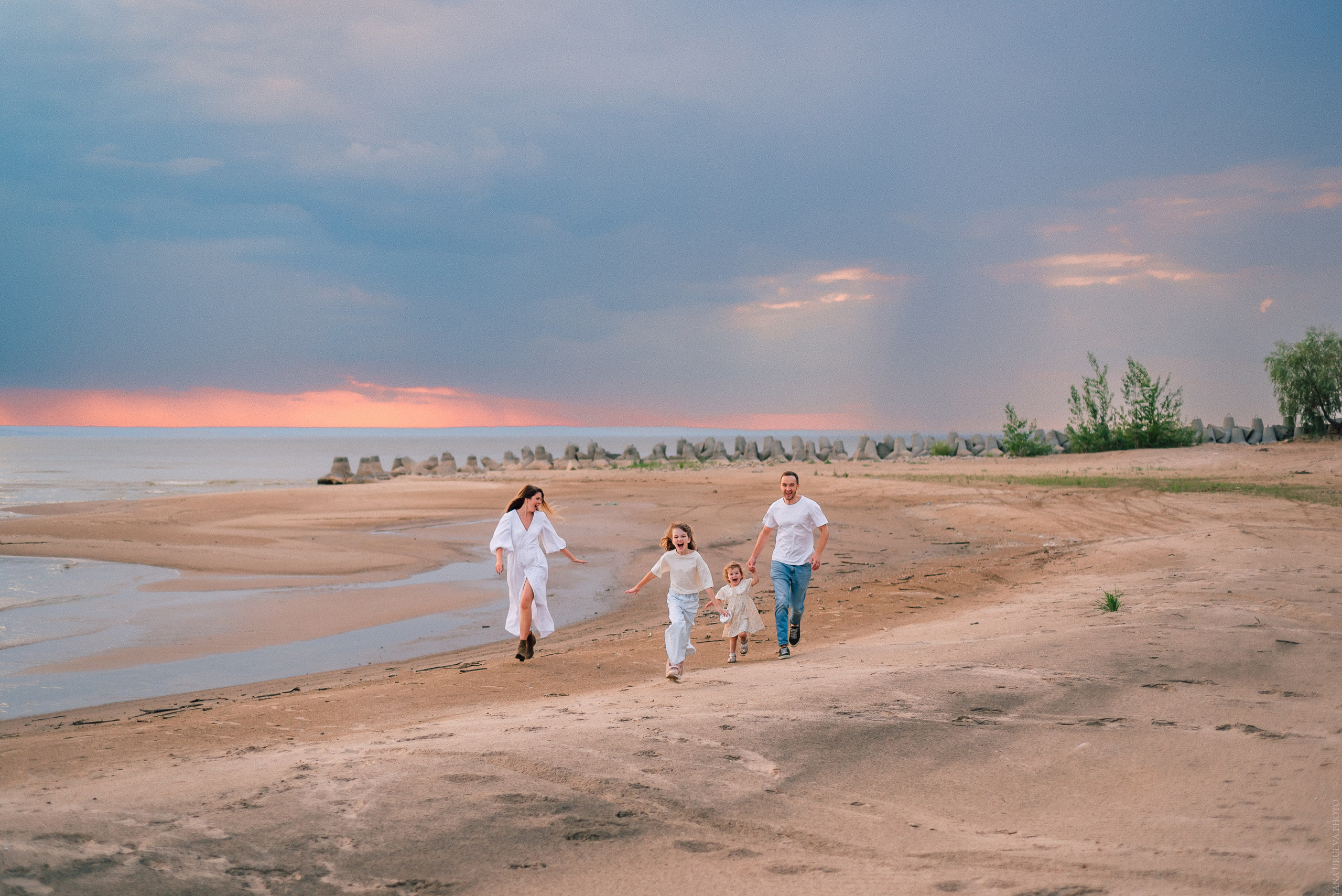 Семья бежит по пляжу на закате