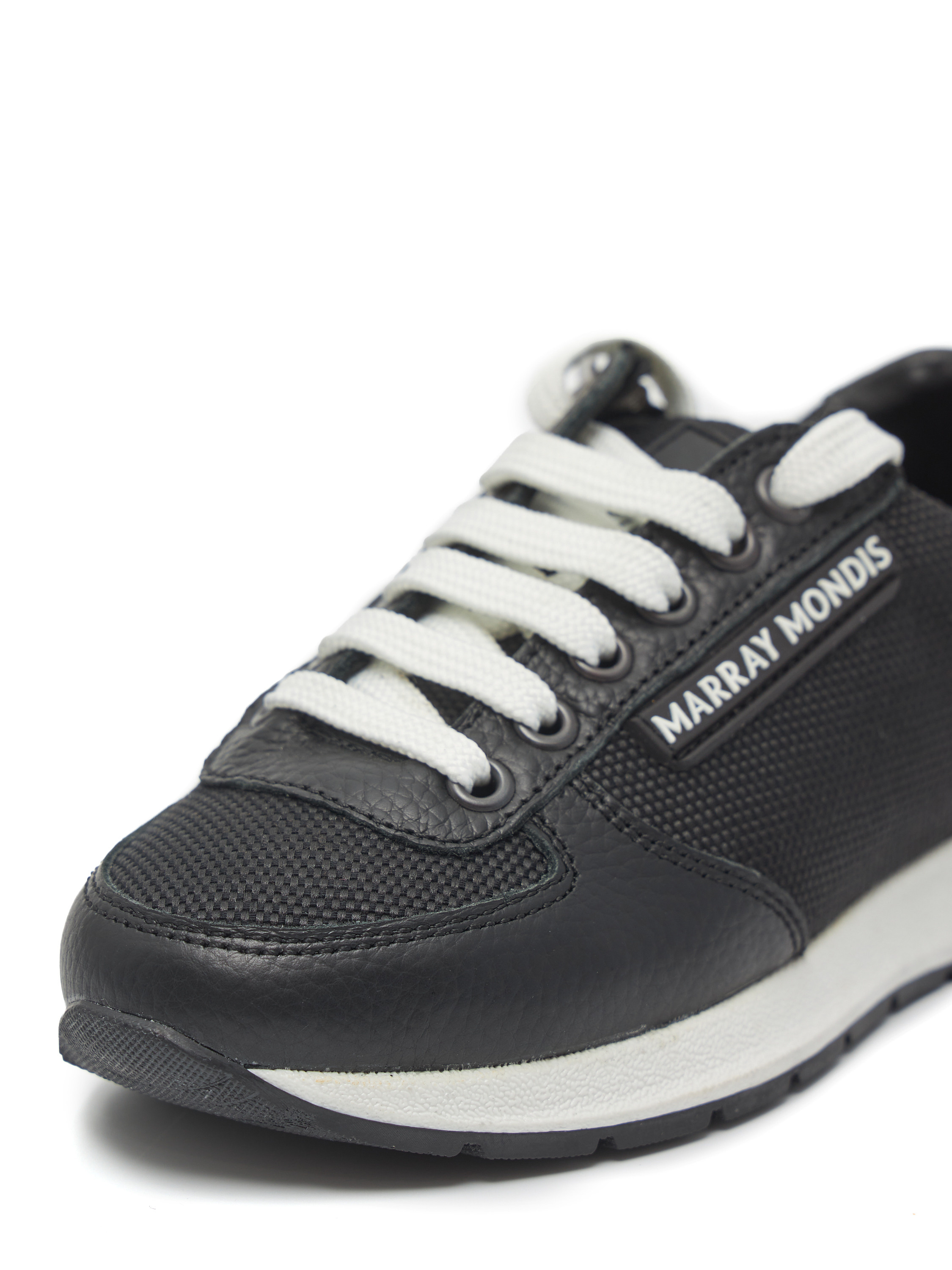 Левый кроссовок черного цвета с белыми шнурками на белом фоне близко