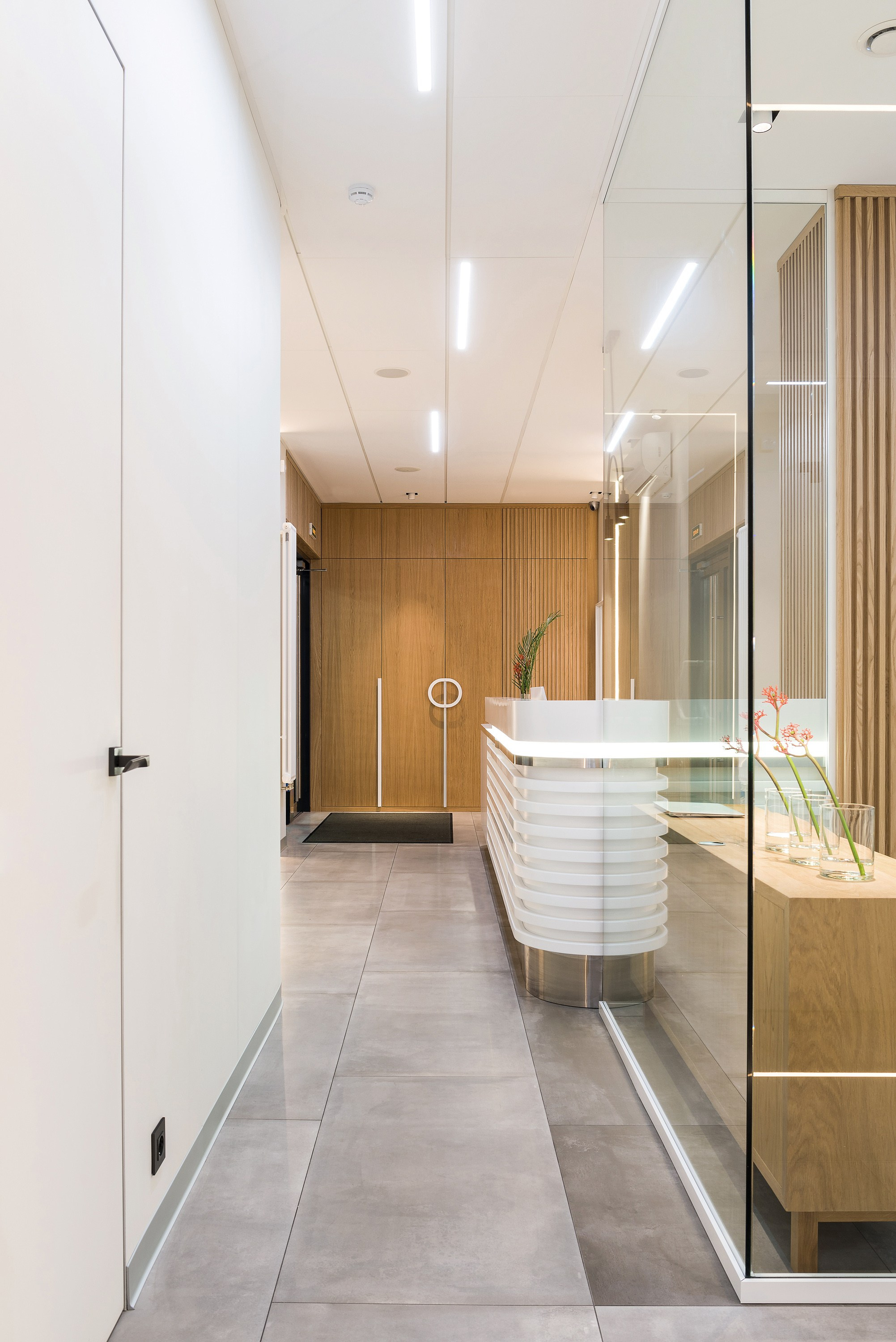 дизайн интерьера стоматологической клиники выполнен в современном минималистичном стиле с теплой домашней атмосферой. Текстуры дерева, наливной пол, яркие акценты, чистота линий, модульная сетка, стеклянные перегородки