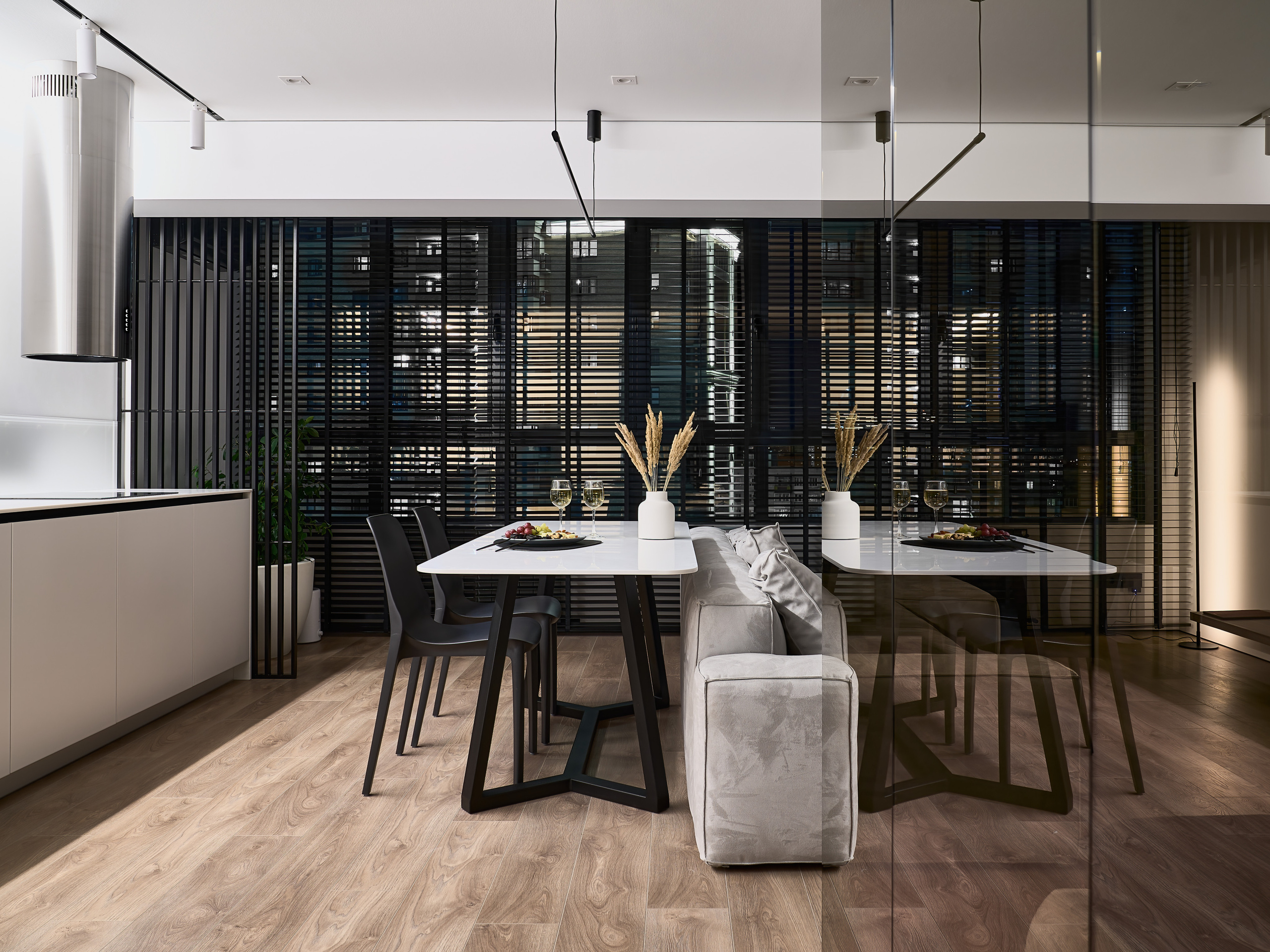 Современная кухня-гостиная с белым столом на черных ножках, серым диваном и стильными черными жалюзи, акцент на гармоничное сочетание дерева и света. Дизайнер Анатолий Котов, интерьер снят фотографом Сергеем Денисенко.