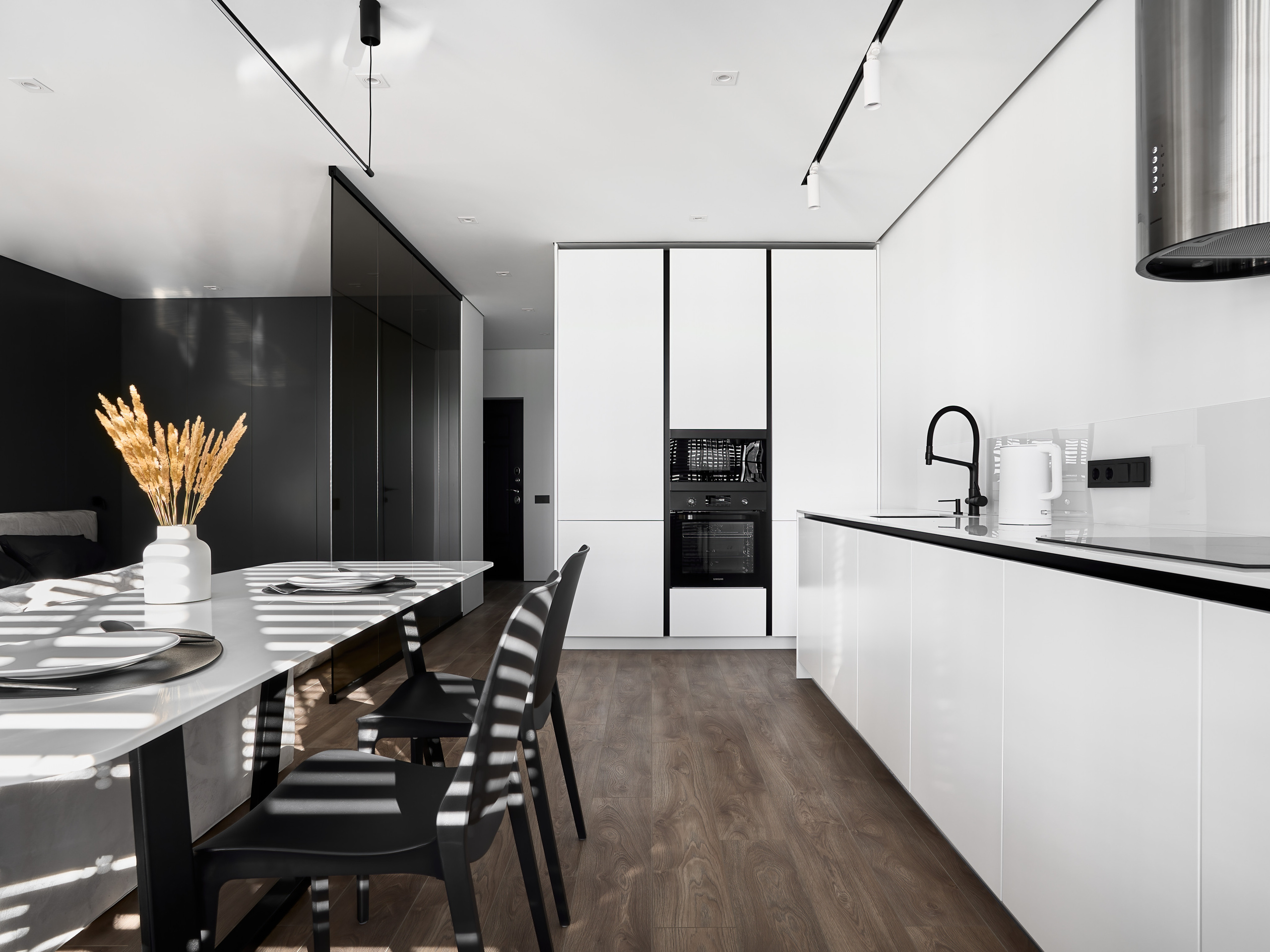 Светлая кухня-столовая с белыми глянцевыми фасадами, встроенной техникой, чёрным смесителем и обеденной зоной с декоративным акцентом из сухих колосьев, дизайн Анатолий Котов, интерьерная фотосъёмка Сергей Денисенко.