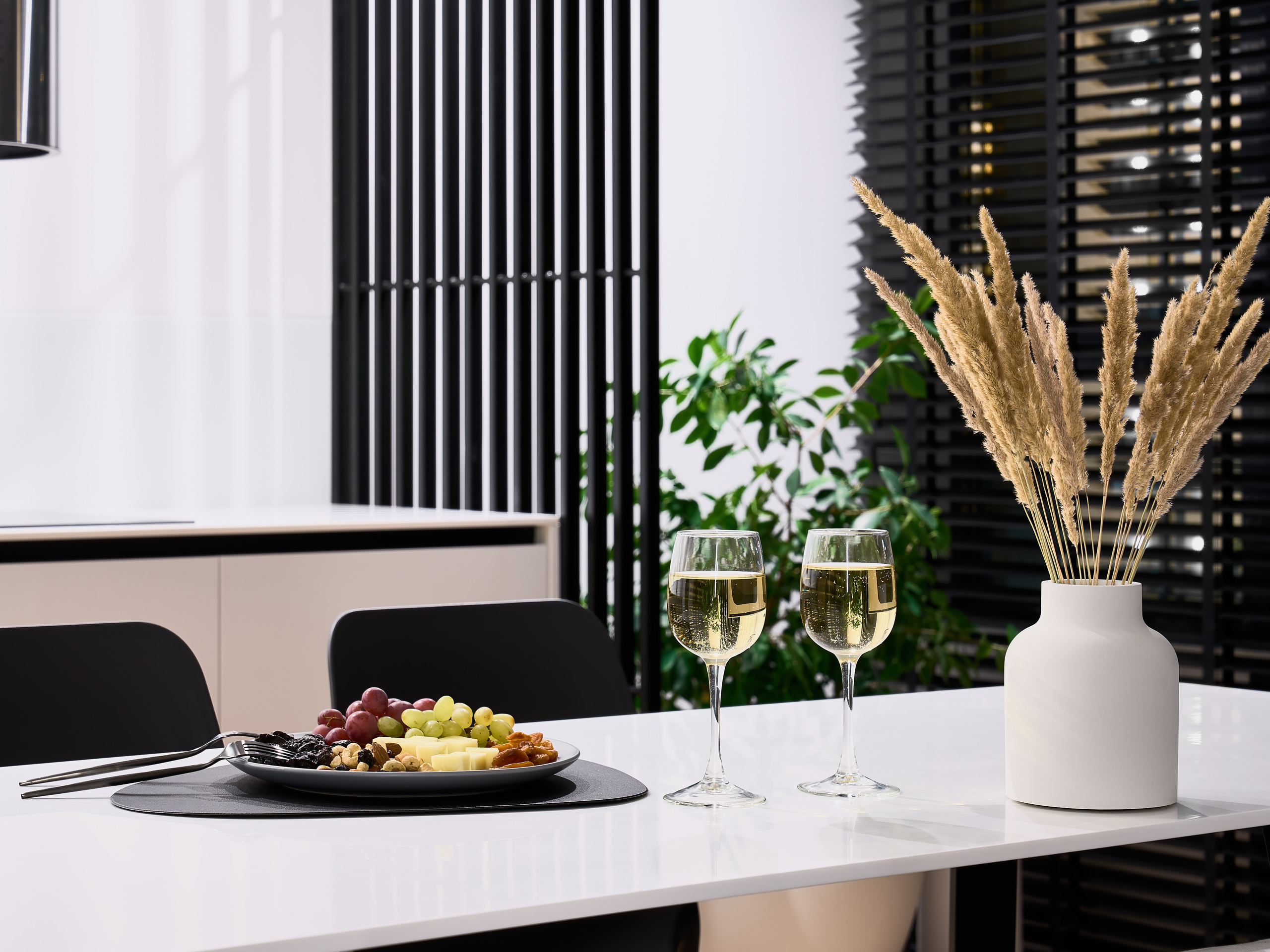Деталь интерьера: белый стол с сервировкой, бокалы с белым вином, тарелка с фруктами и орехами, декор в виде вазы с сухоцветами. Современный стиль от дизайнера Анатолия Котова, съемка фотографа Сергея Денисенко.